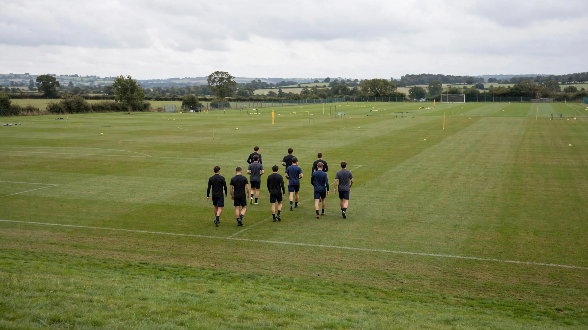 Soccer players in plain dark training kits walking across a grass training field