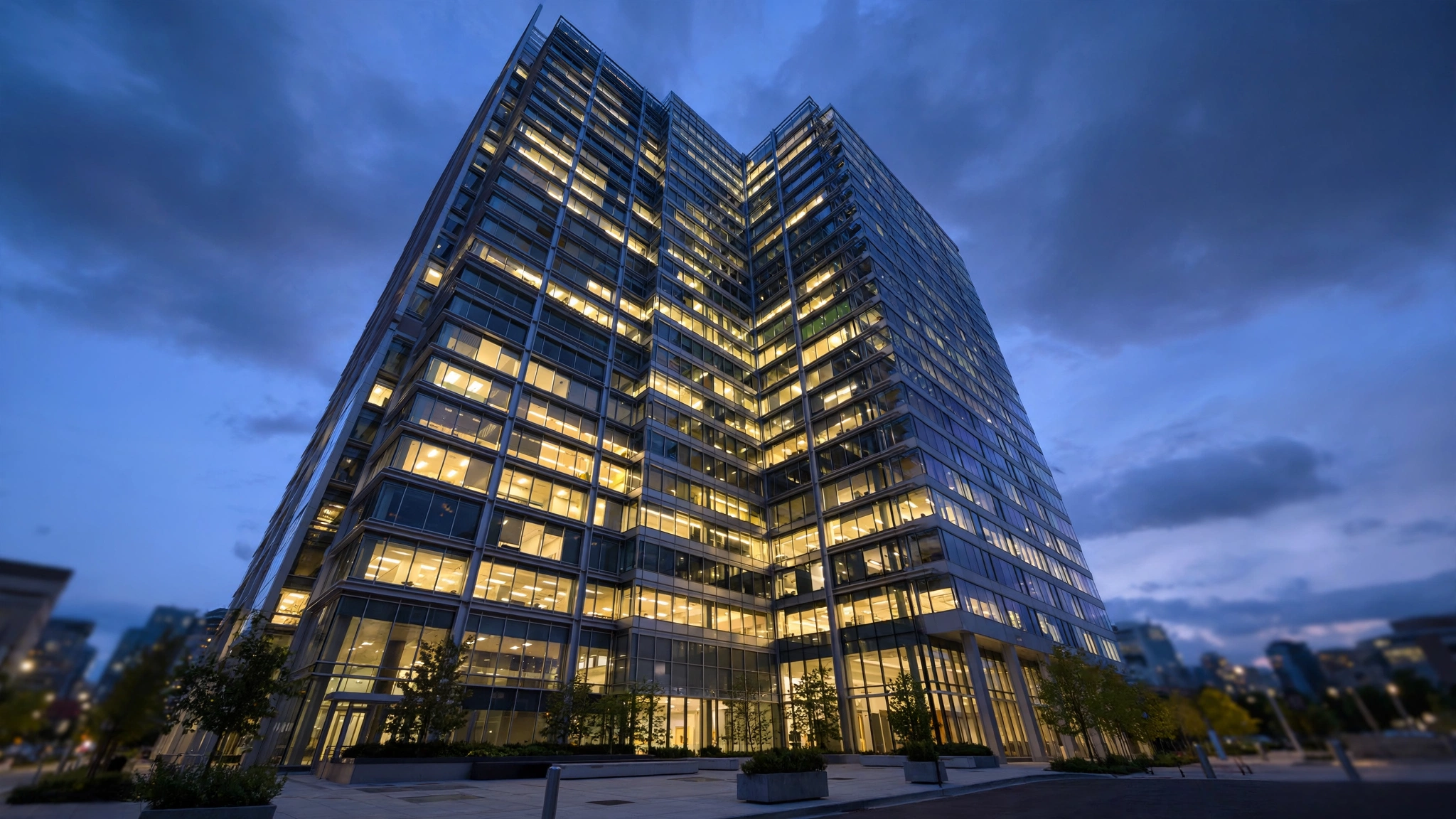 A modern glass office tower with lit windows at dusk