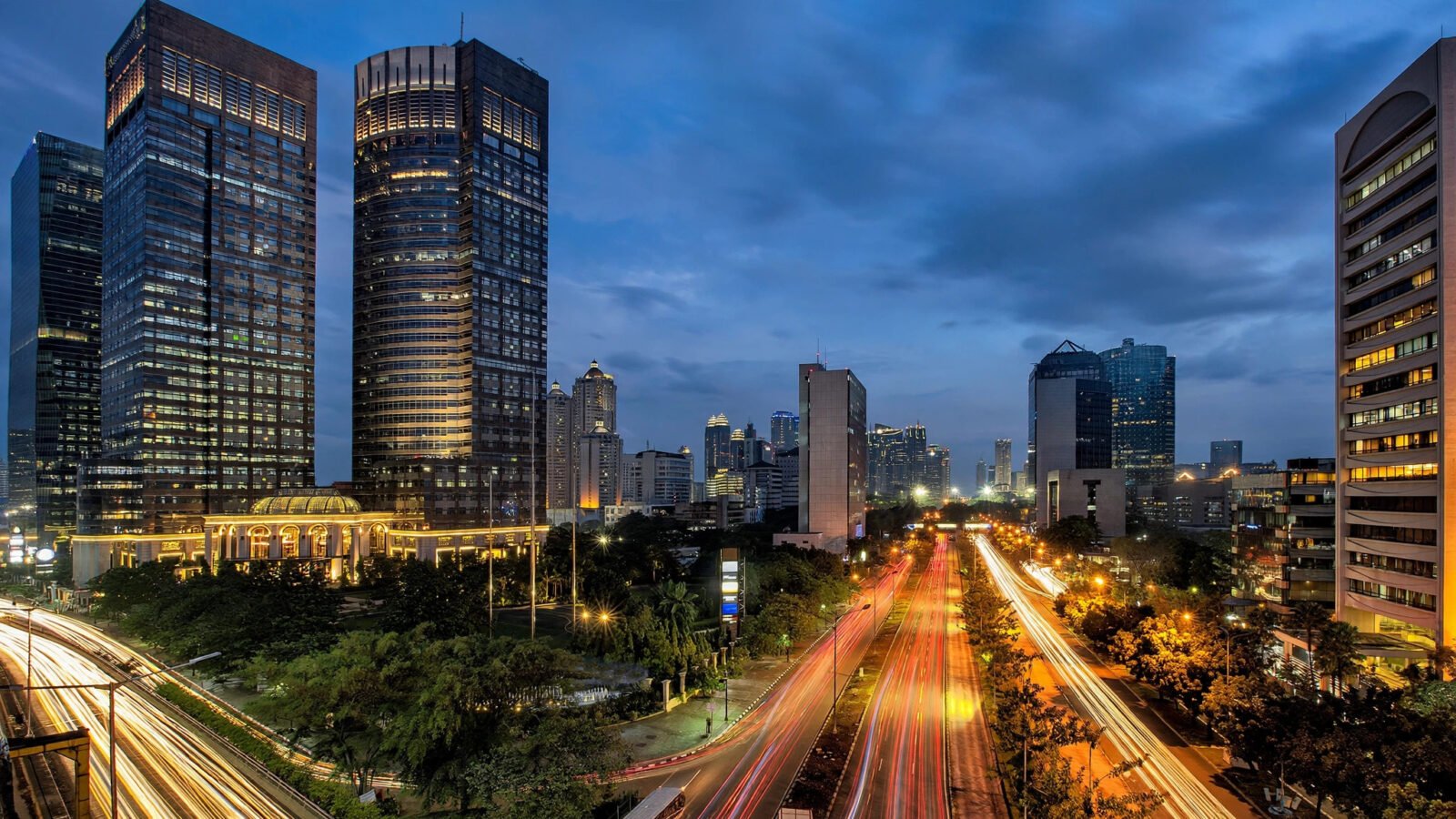 Jakarta's financial district skyline at dusk with illuminated office towers and light trails from traffic