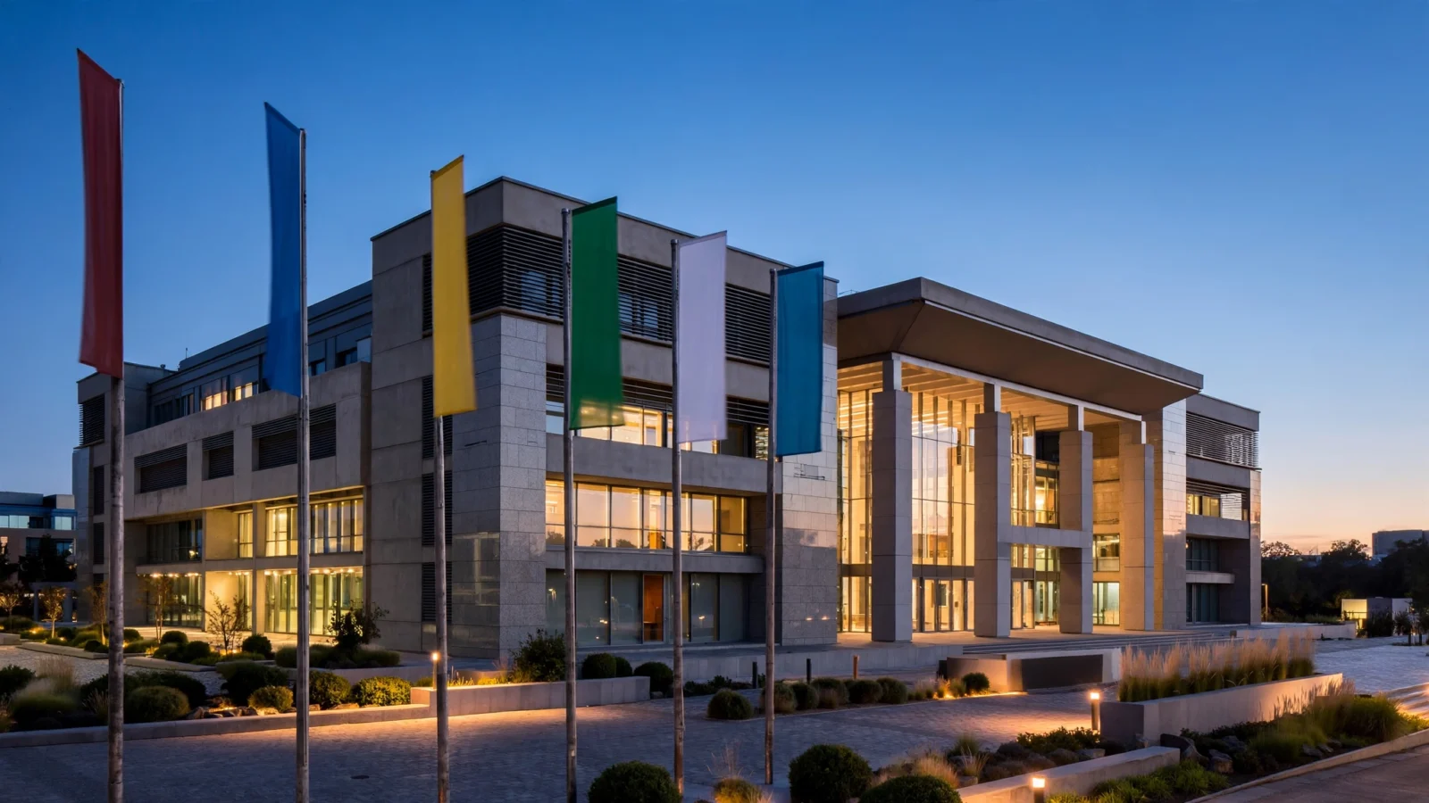 A modern government building exterior at dusk with flags in front.