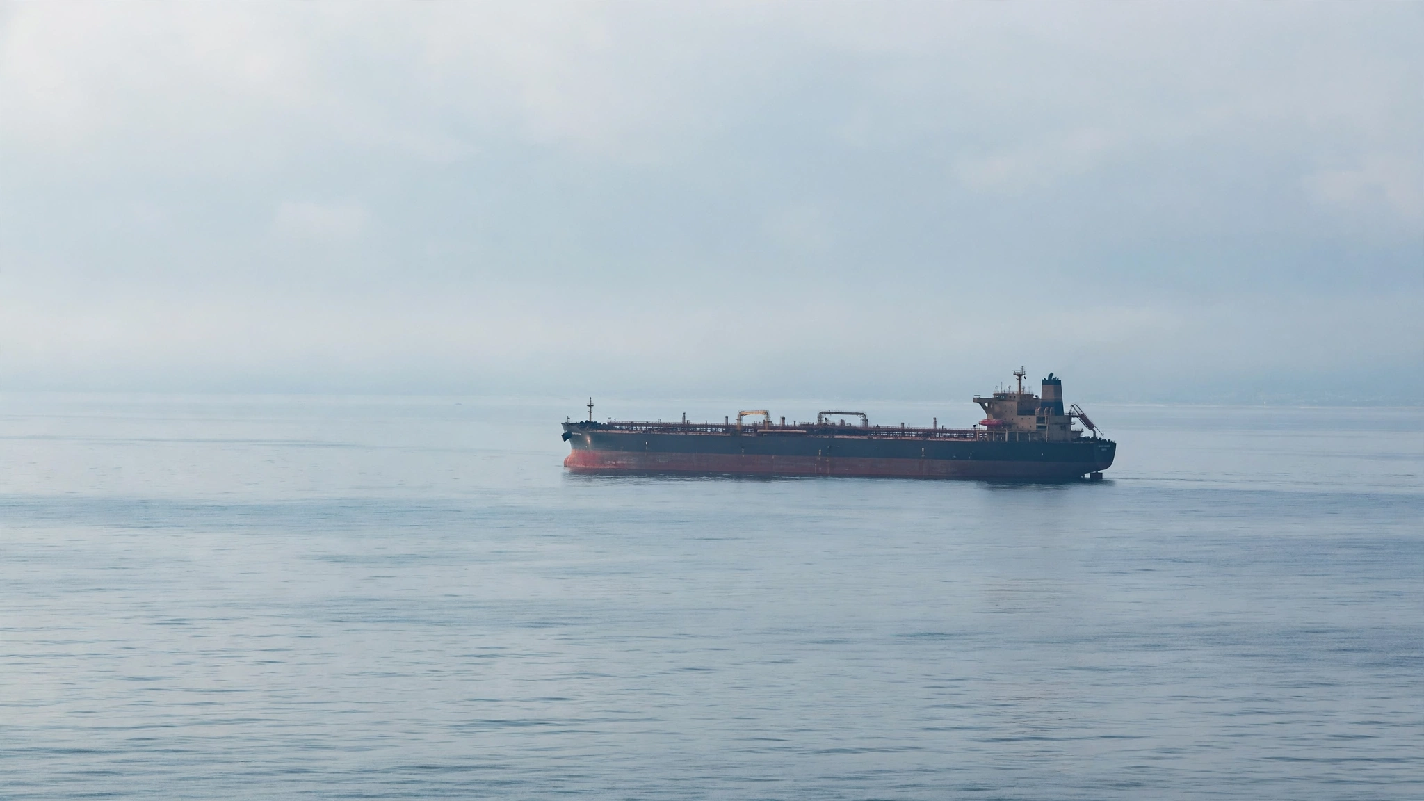 A supertanker oil ship on calm open water under a hazy sky