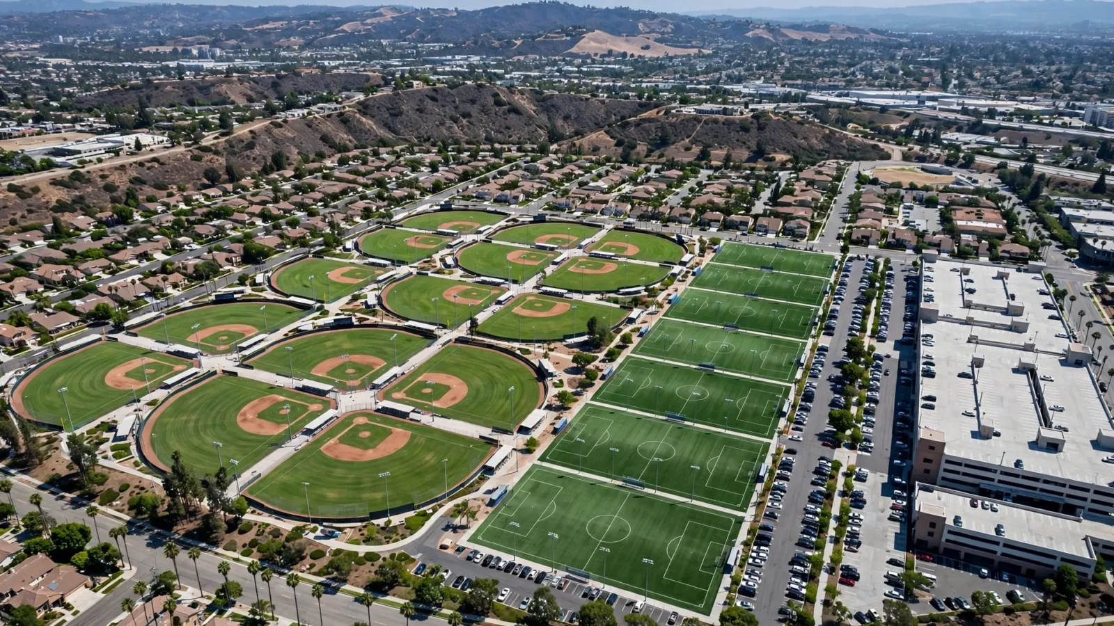 An aerial view of a large sports complex with baseball diamonds, soccer fields and a parking structure