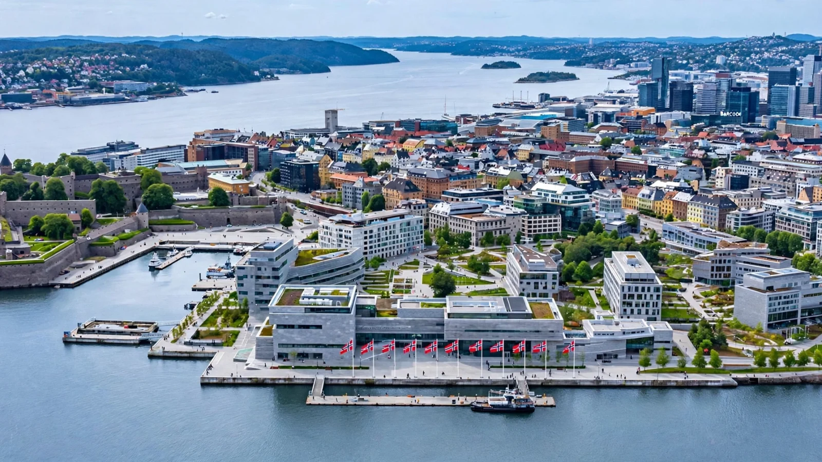 Aerial view of the Oslo waterfront and government quarter with Norwegian flags on a building, overlooking the calm fjord