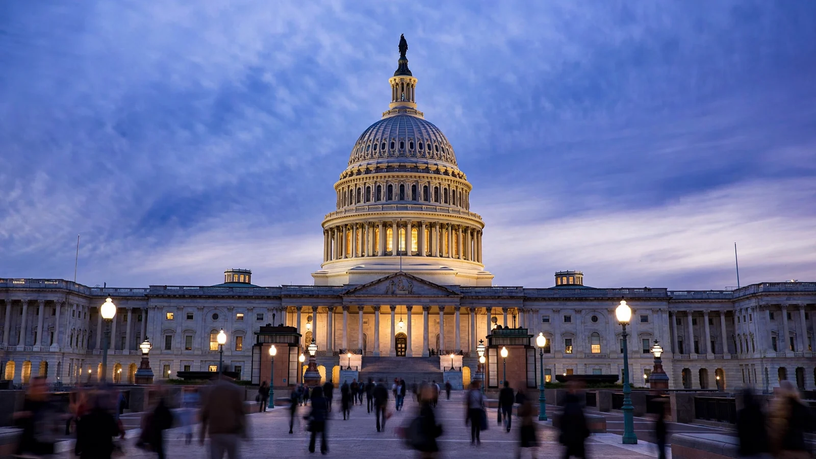 United States Capitol building illuminated at dusk with pedestrians walking in the foreground