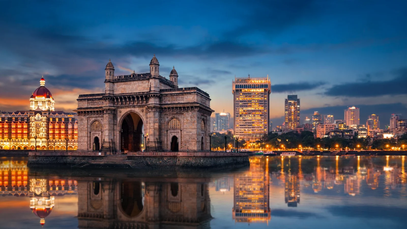 A stone arch monument on the Mumbai waterfront at dusk with city lights reflected in the water.