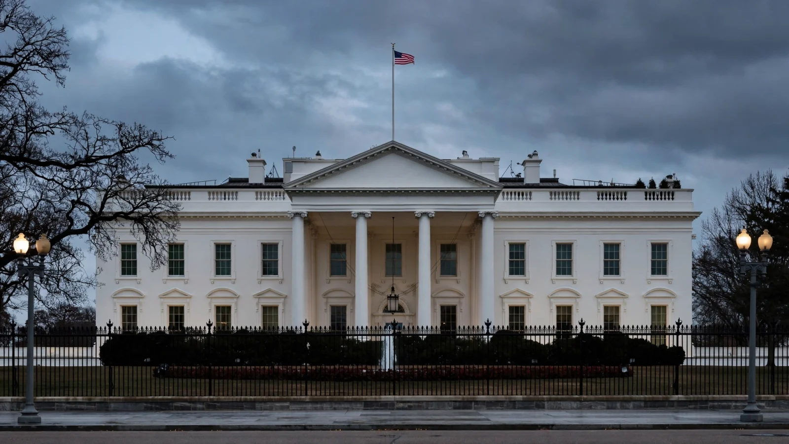 The White House at dusk in Washington, D.C., with the American flag flying above the north facade.