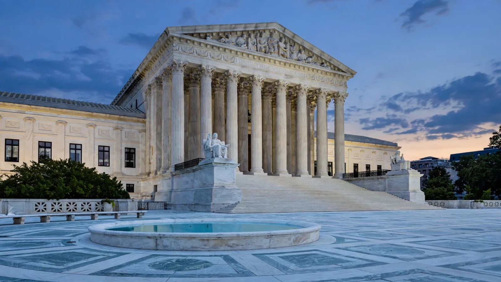 The U.S. Supreme Court building at dusk, with marble columns, wide steps and a circular pool in the plaza