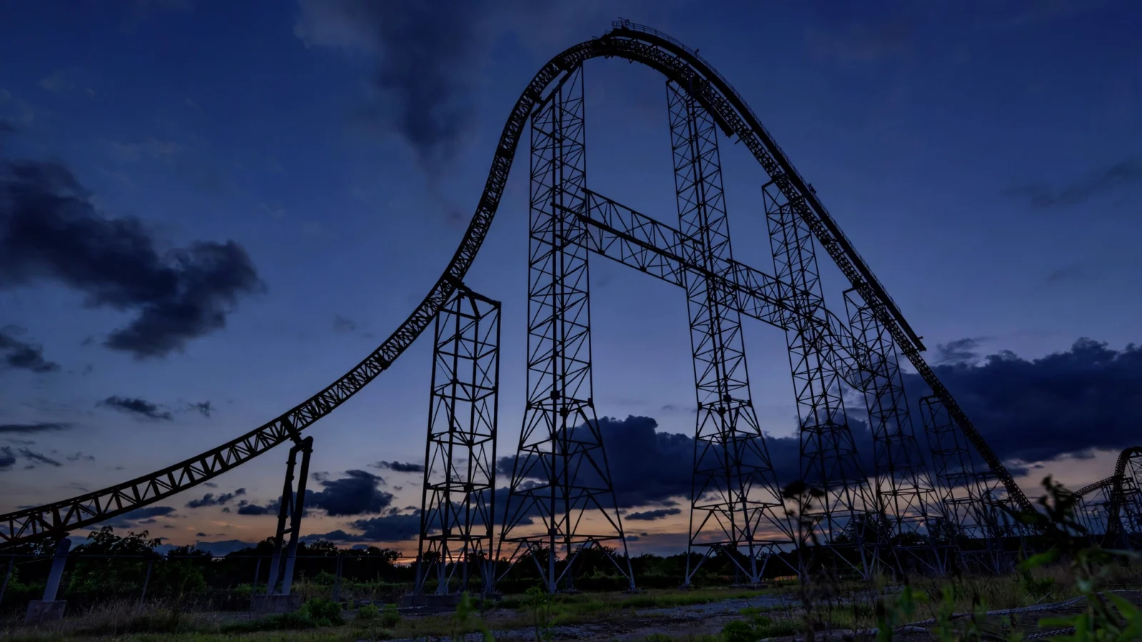 Steel roller coaster track silhouetted against a dusky evening sky