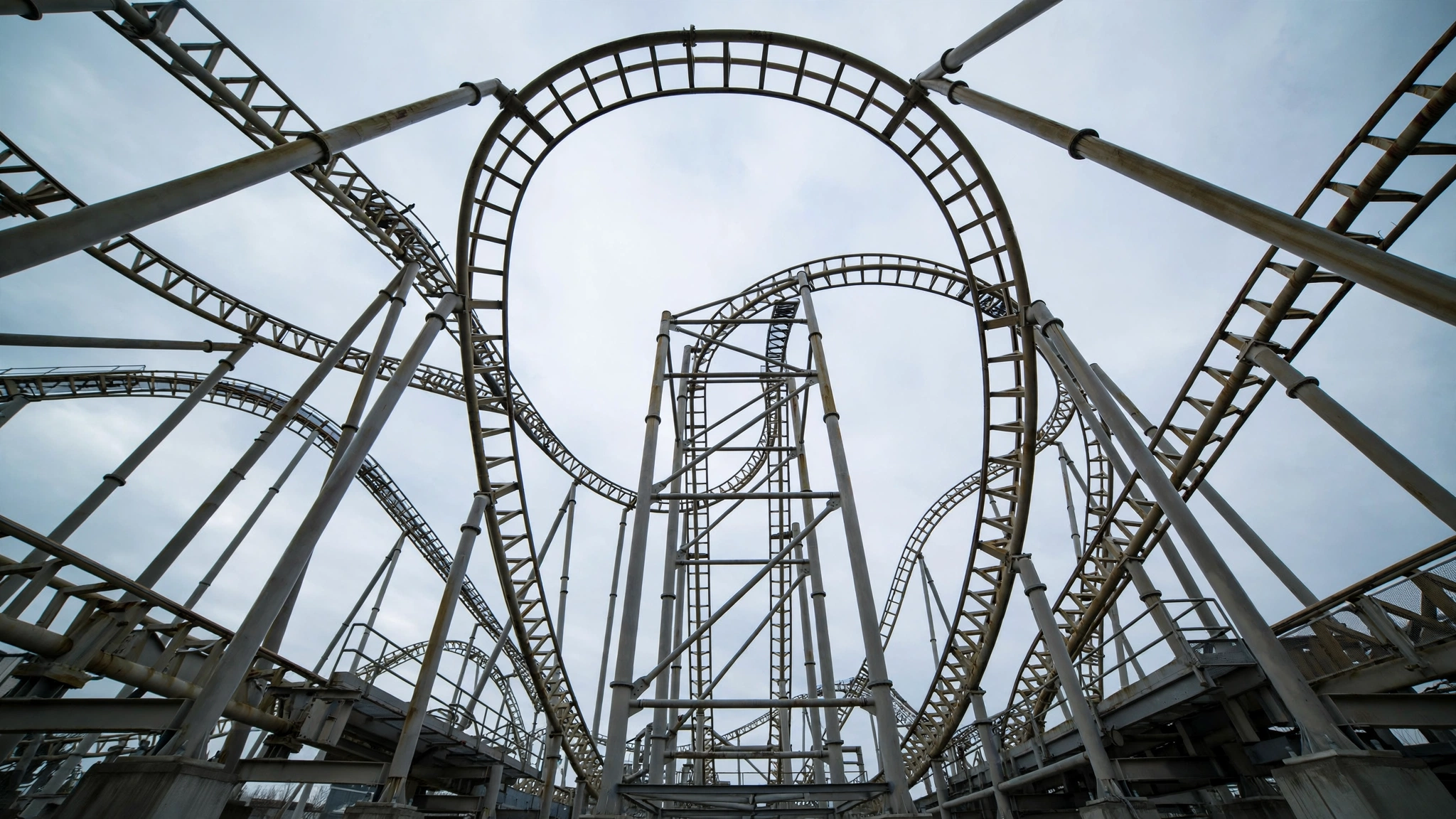View looking up at steel roller coaster track and support columns against a pale sky