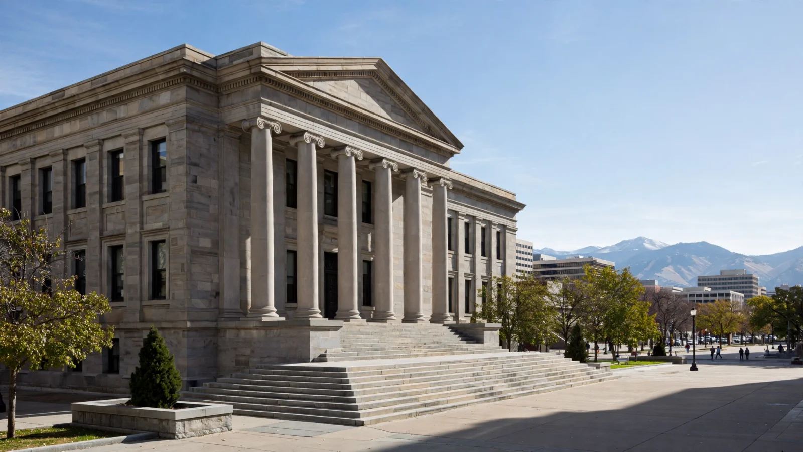 A stone courthouse building with tall columns and wide steps under a clear sky, with mountains in the distance.