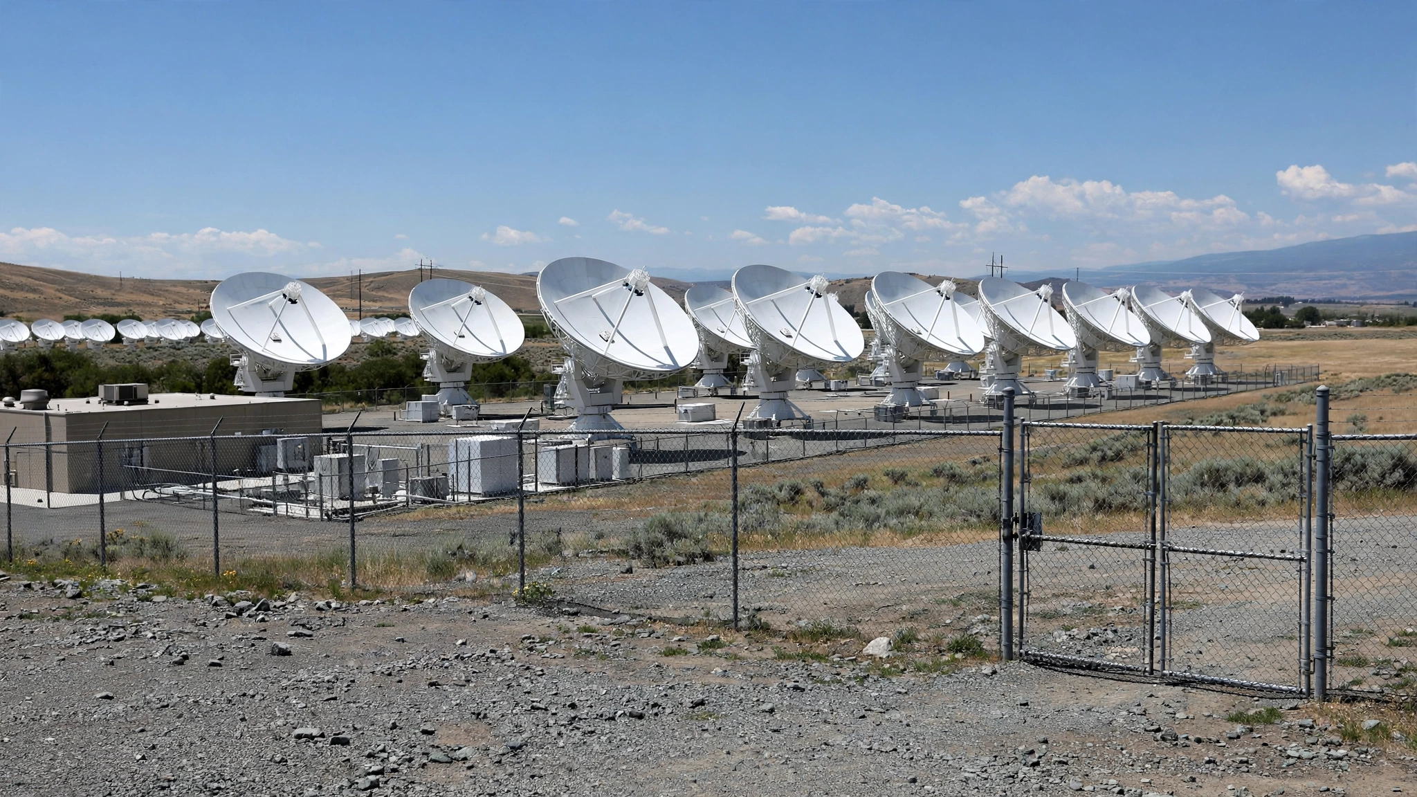 Rows of large white satellite dish antennas in a fenced lot under a blue sky