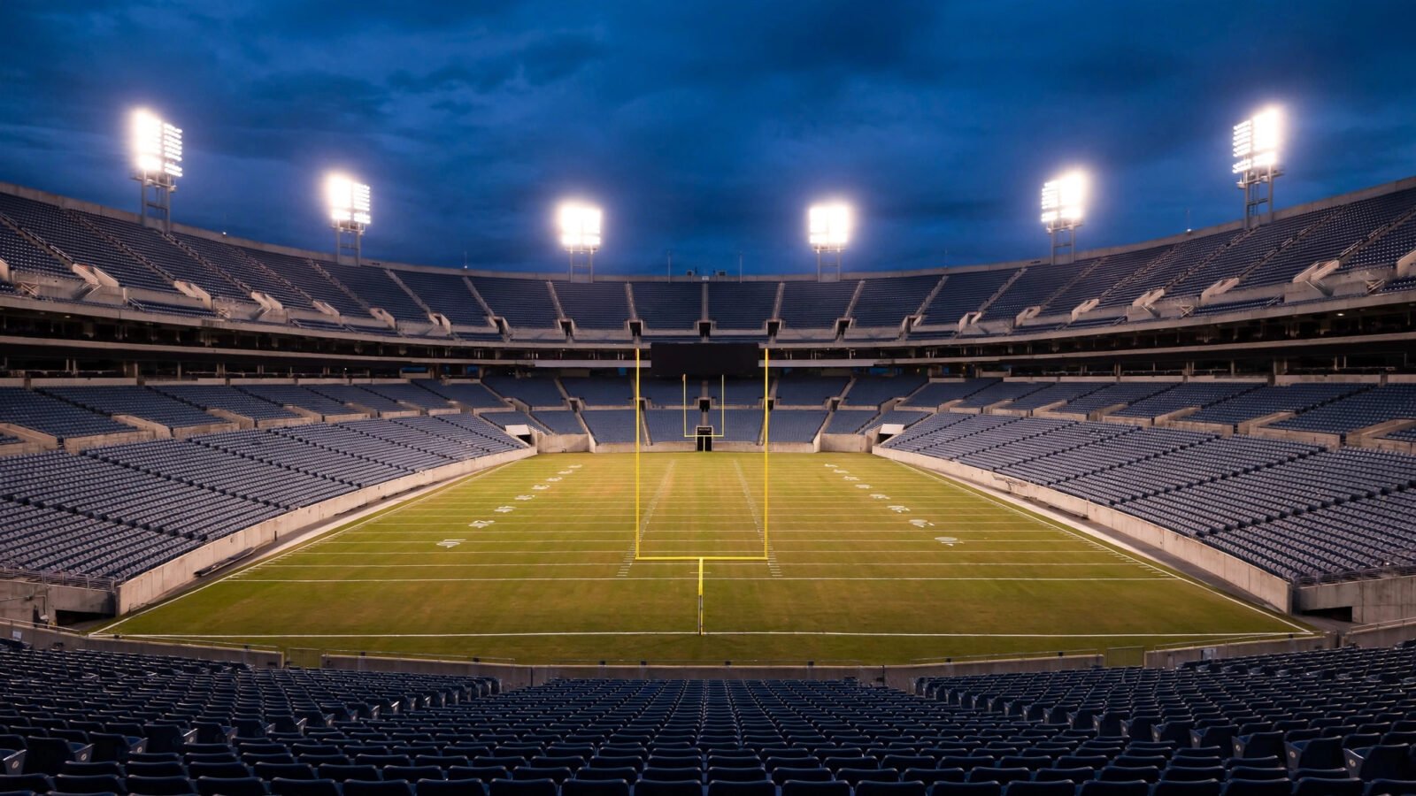 An empty professional football stadium lit by floodlights at night.