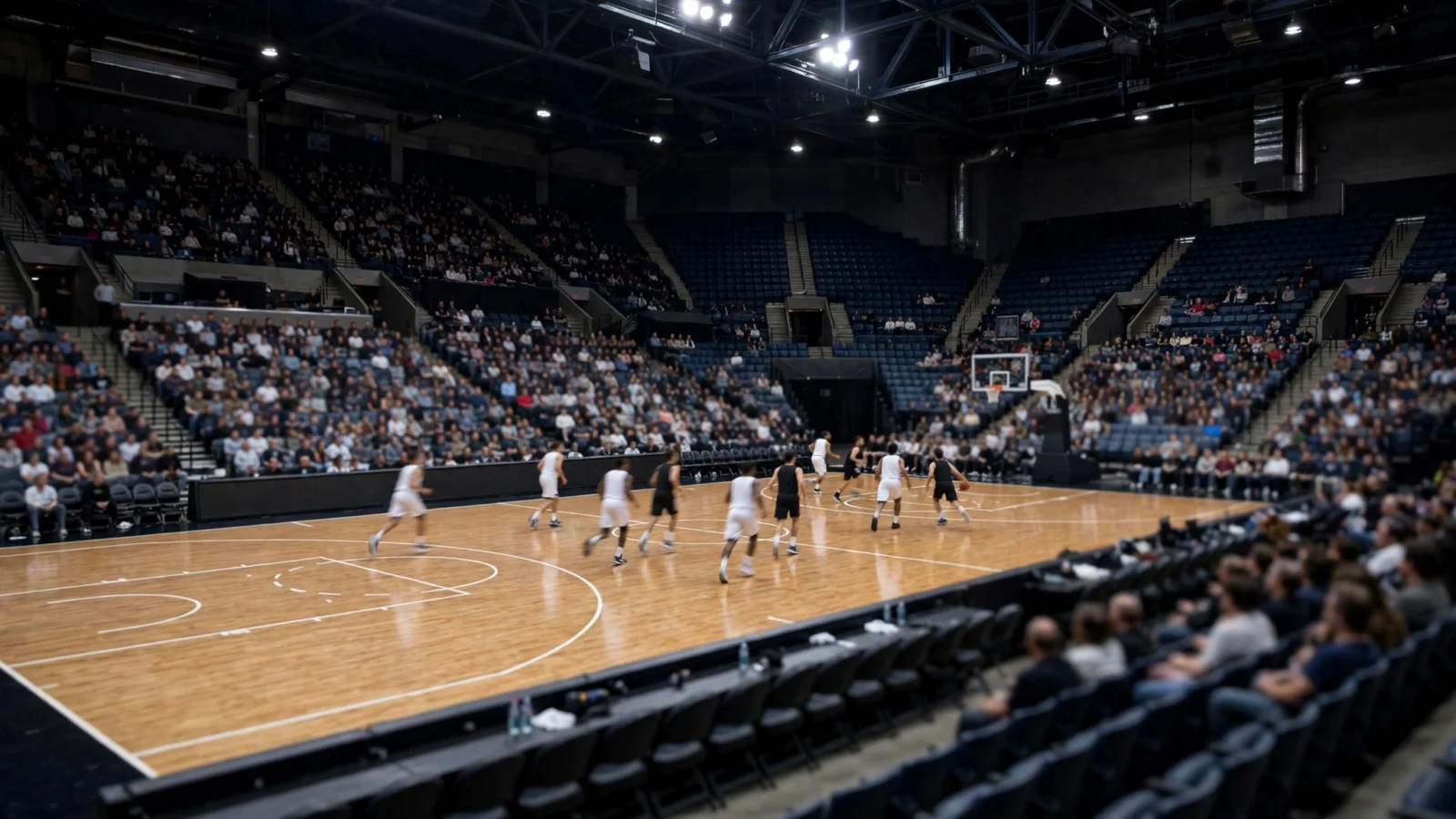 Basketball players in plain white and black uniforms playing on a polished court in a large arena filled with spectators