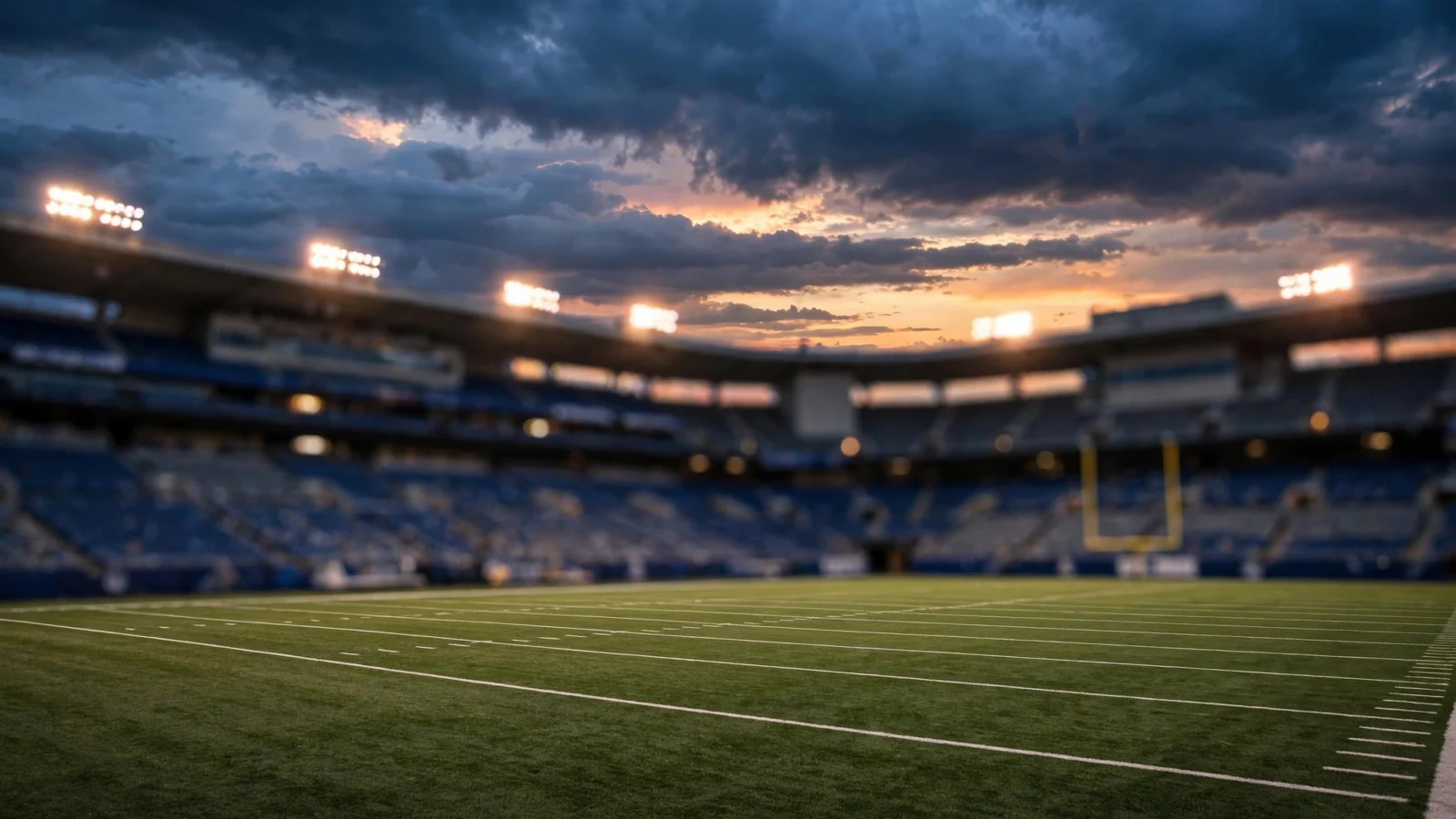An empty American football stadium at dusk with floodlights on and a dramatic cloudy sky