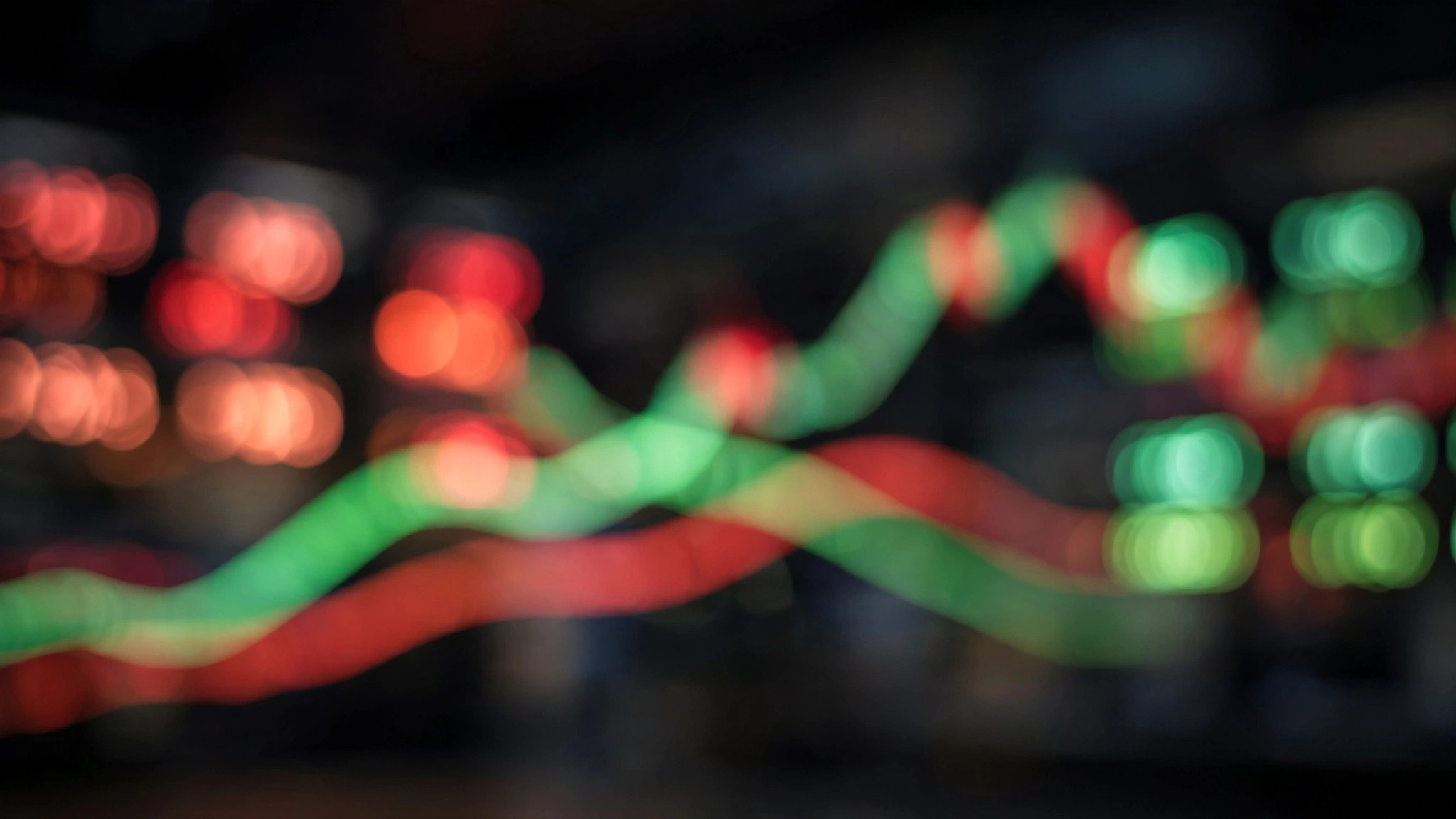 A blurred stock market display board with out-of-focus red and green charts