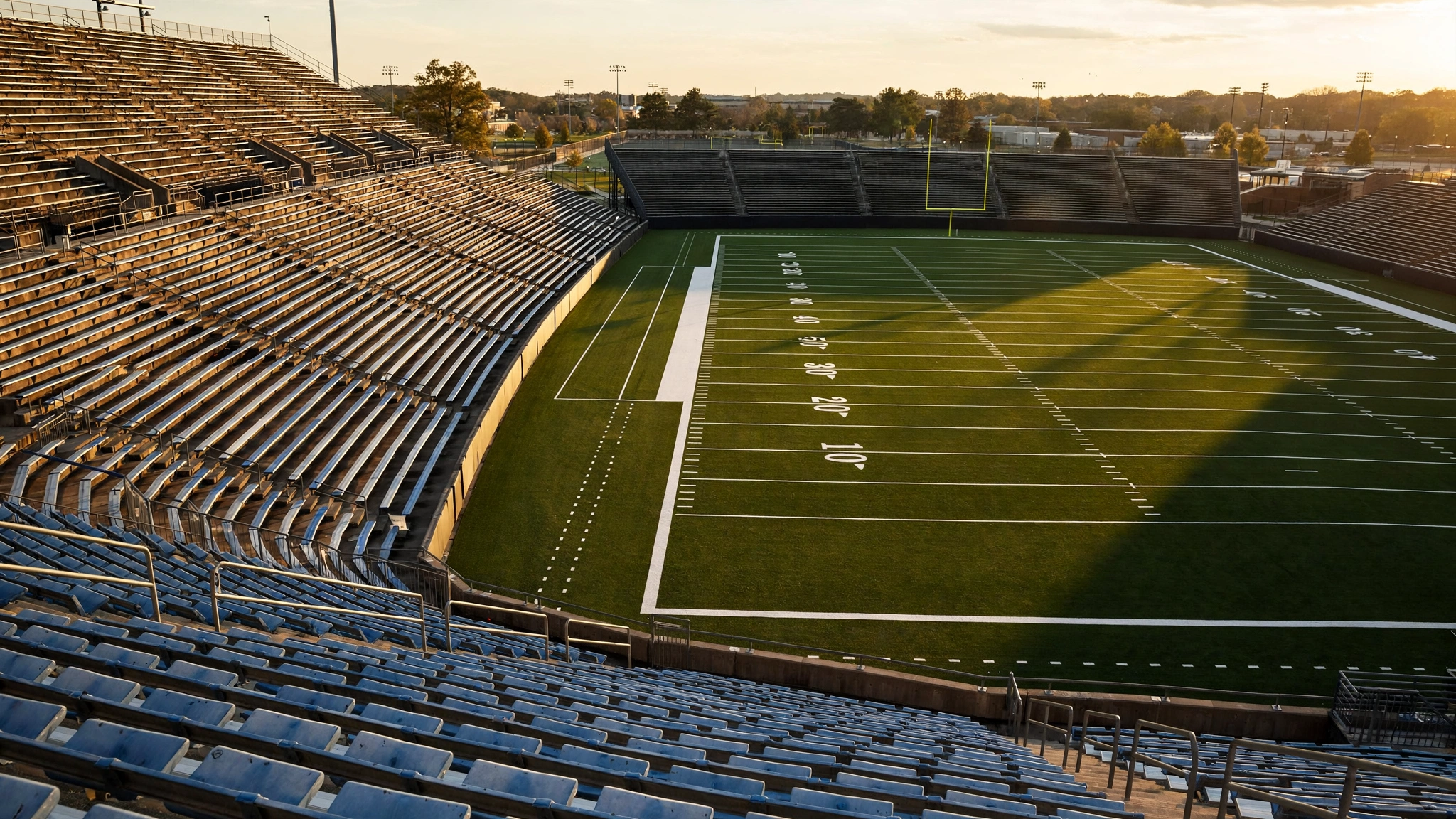 An empty college football field with yard lines and goal posts, seen from the stands in late afternoon light.