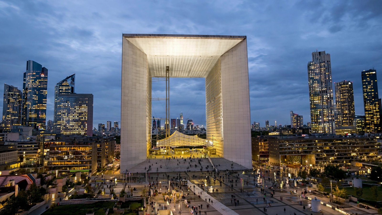 The illuminated Grande Arche and office towers of the La Defense business district in Paris at dusk.
