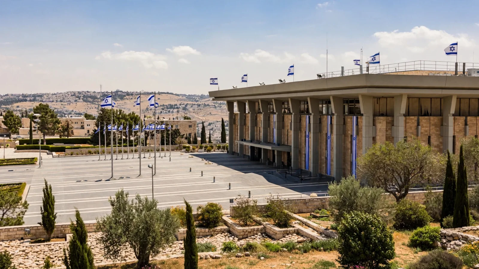 The Knesset building in Jerusalem with rows of Israeli flags flying in front on a clear day