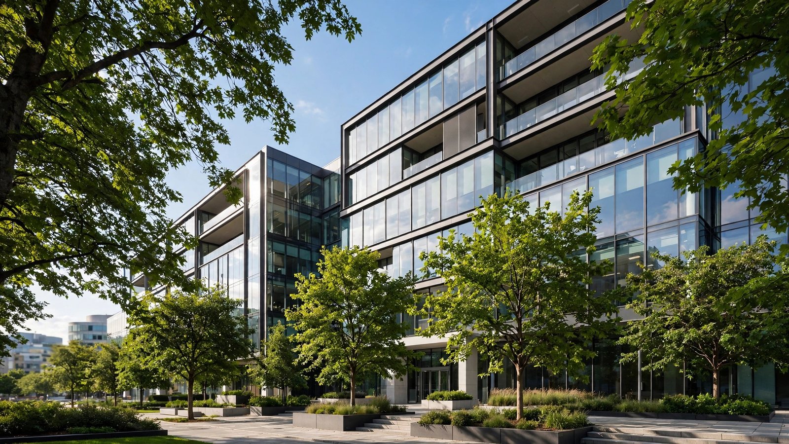 A modern glass office building with green trees in front on a sunny day