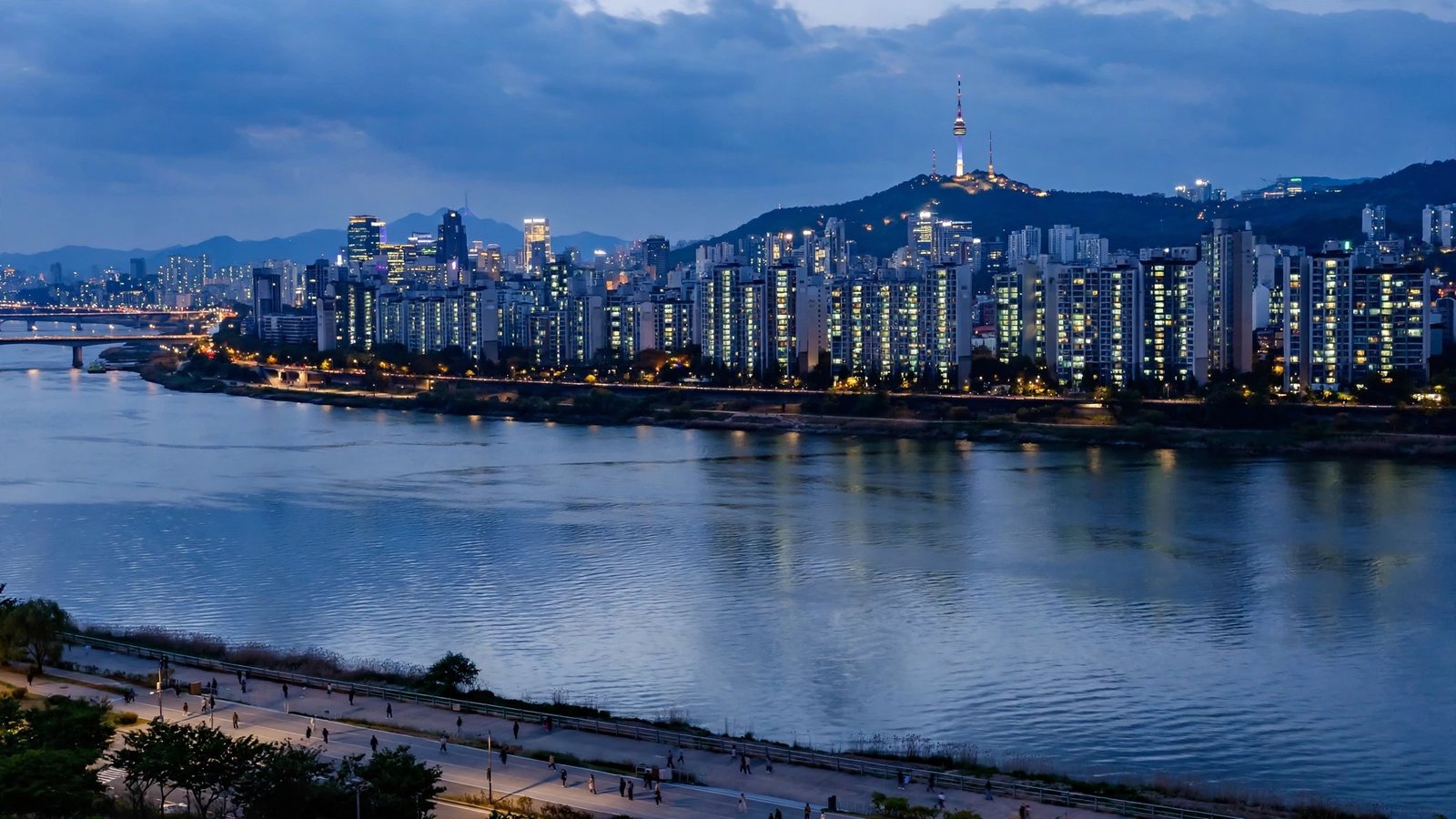 A city skyline at dusk with lit apartment towers along a wide river