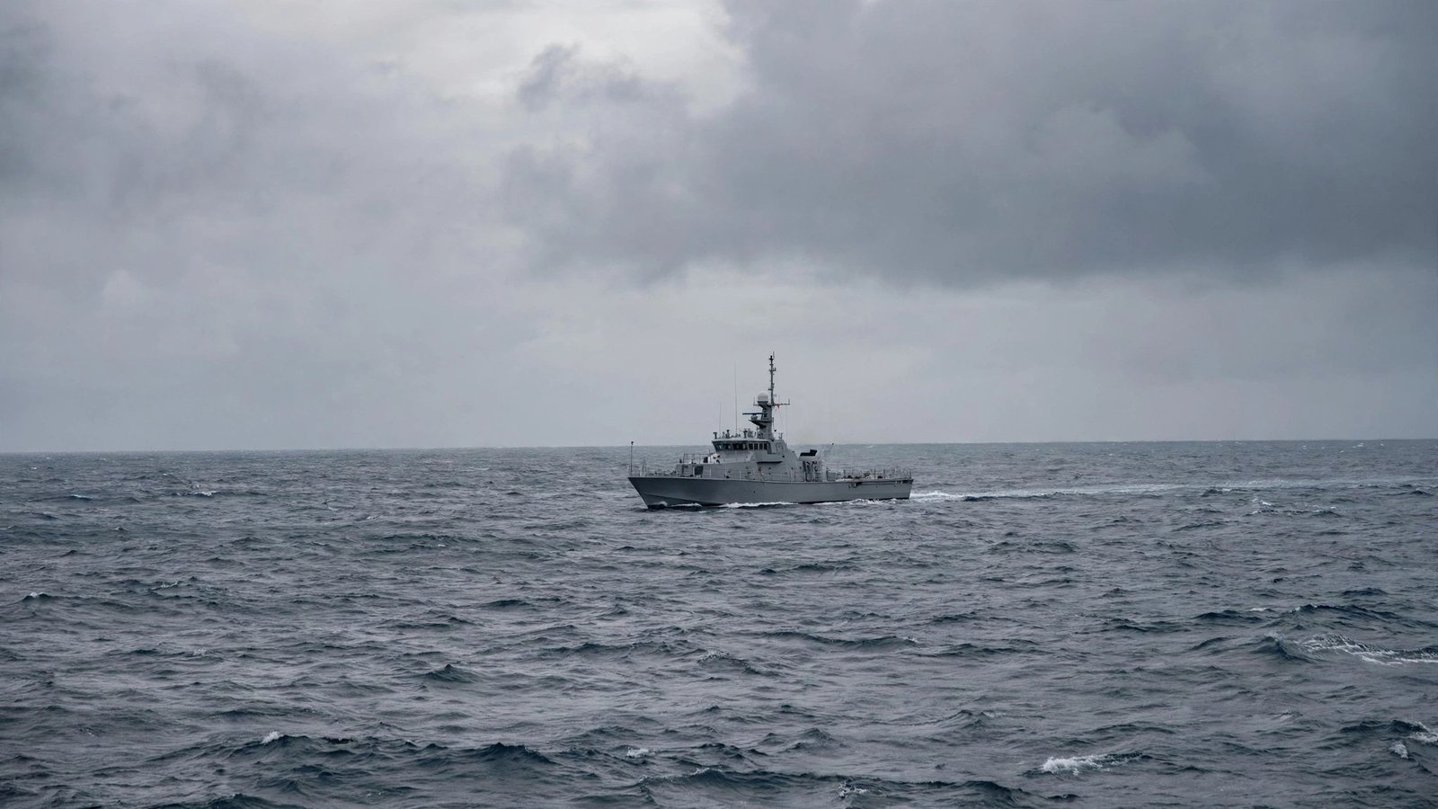 A grey patrol ship sailing on open sea under a cloudy sky