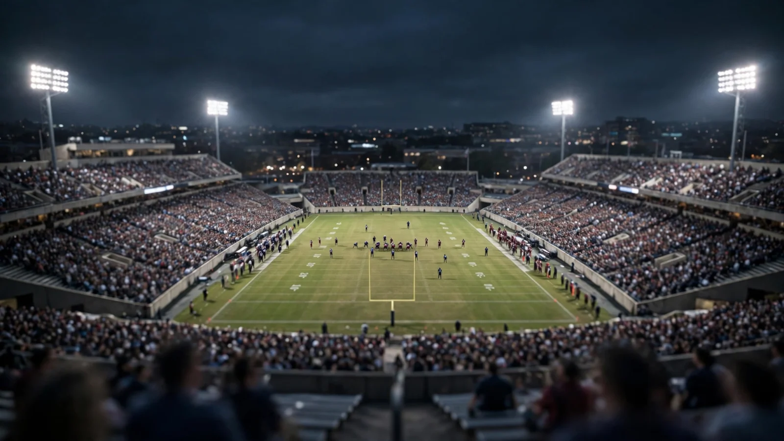 A crowded American football stadium at night with floodlights illuminating the field and distant players