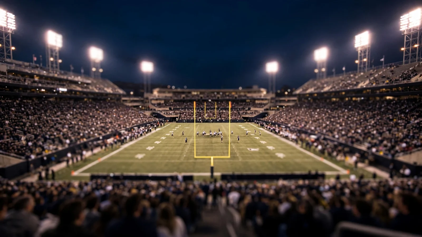 A college football stadium lit up at night with goalposts and players on the field.
