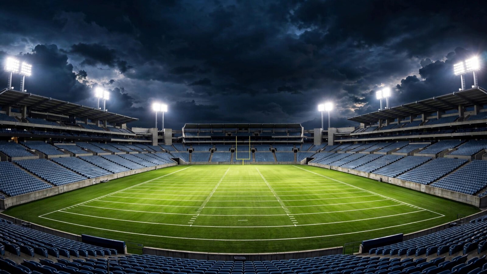 An empty American football stadium at night with the field lit under floodlights.