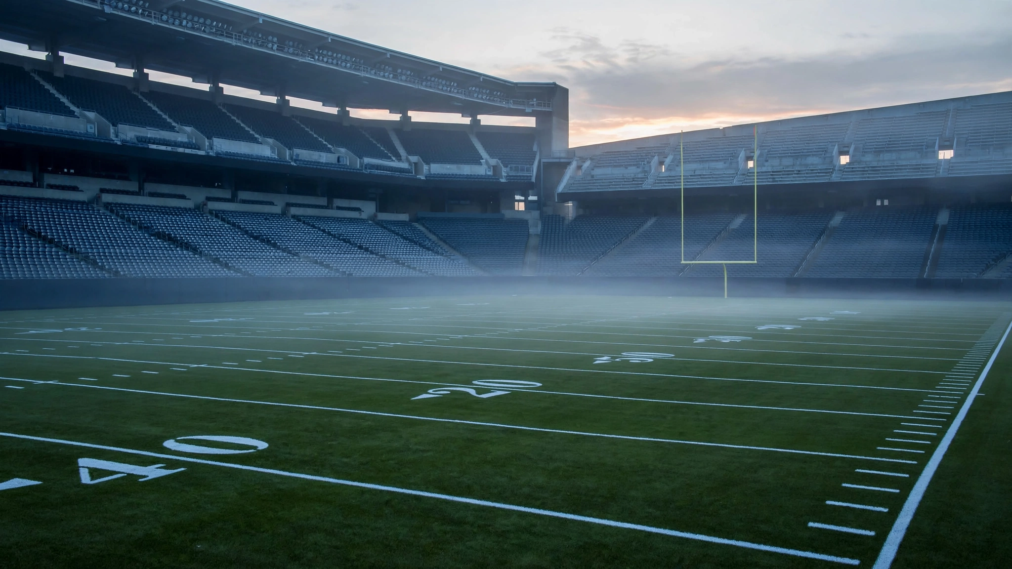 An empty football stadium field with yard lines and goalposts at dawn