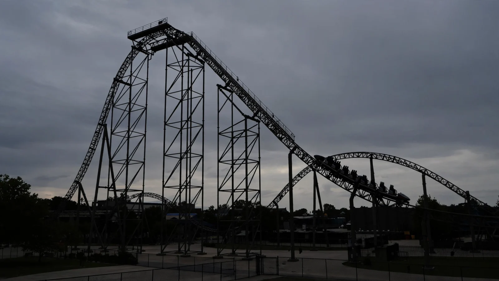 A tall steel roller coaster silhouetted against a cloudy evening sky
