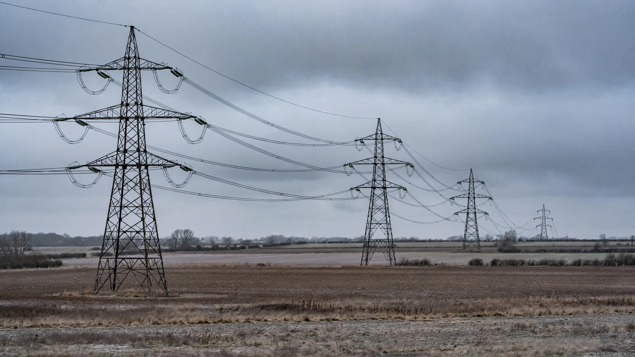 High-voltage power transmission towers and lines stretching across fields under an overcast sky