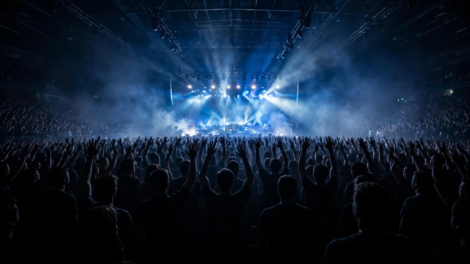 A crowded concert arena with bright stage lights and raised hands in the audience