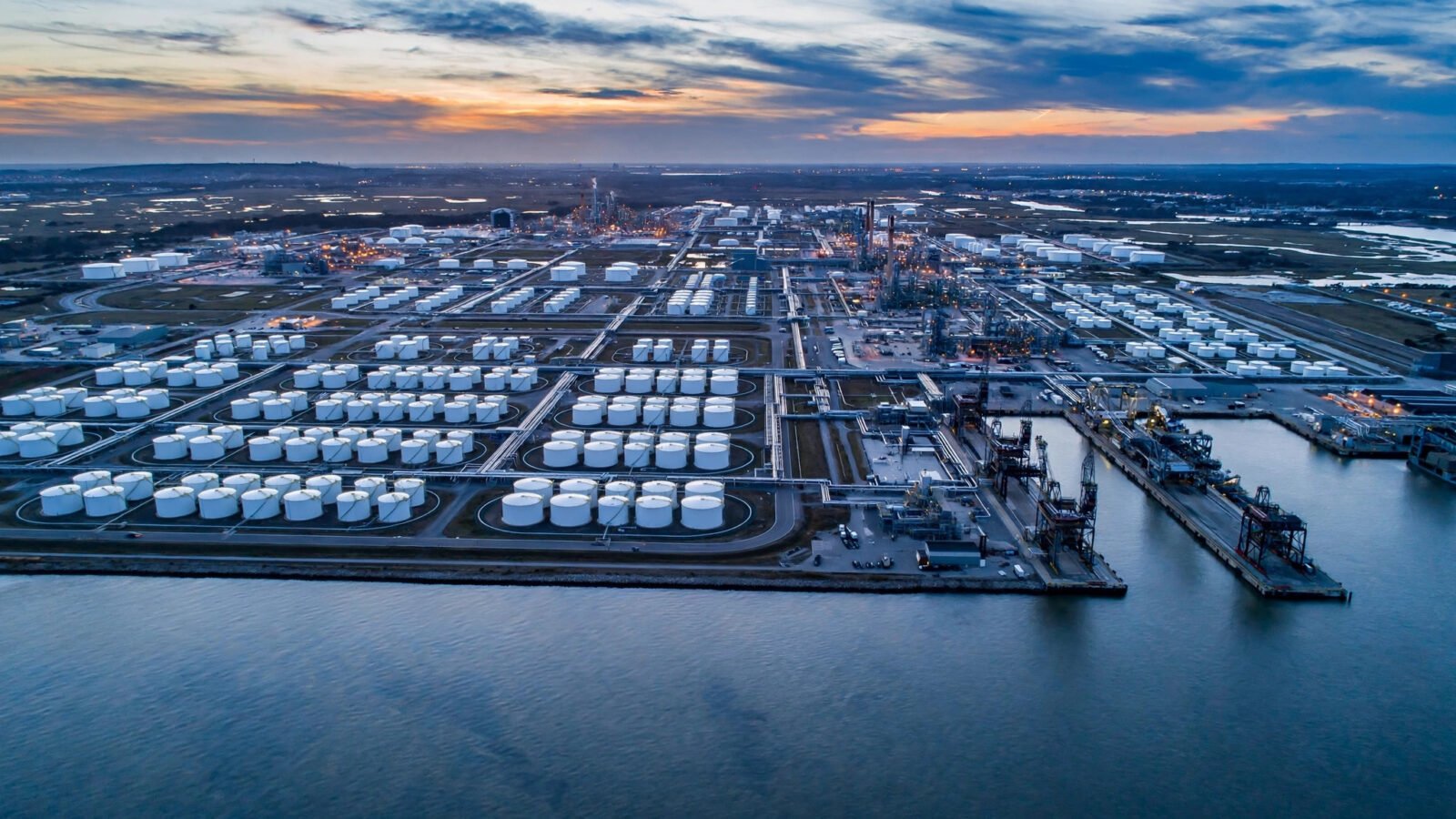 Aerial view of a large oil terminal with rows of white storage tanks at dusk
