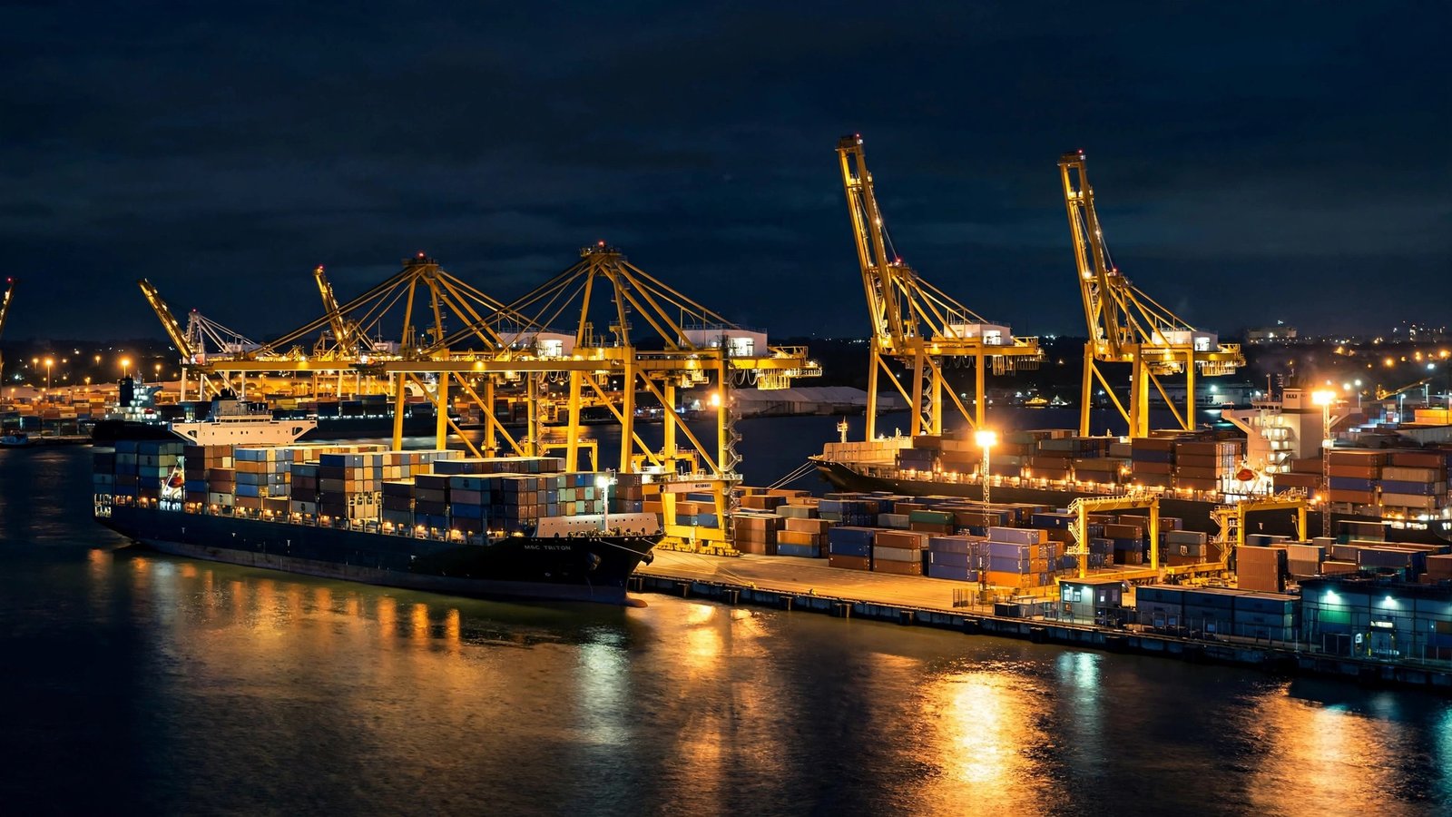 A cargo port at night with container ships, cranes and stacked shipping containers