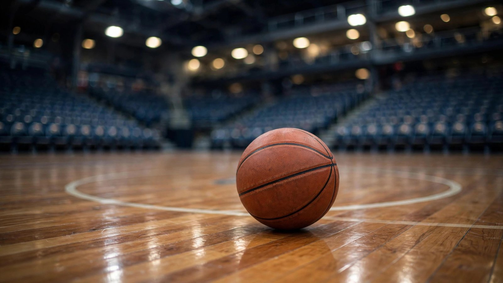 A basketball resting on a polished hardwood court in an arena