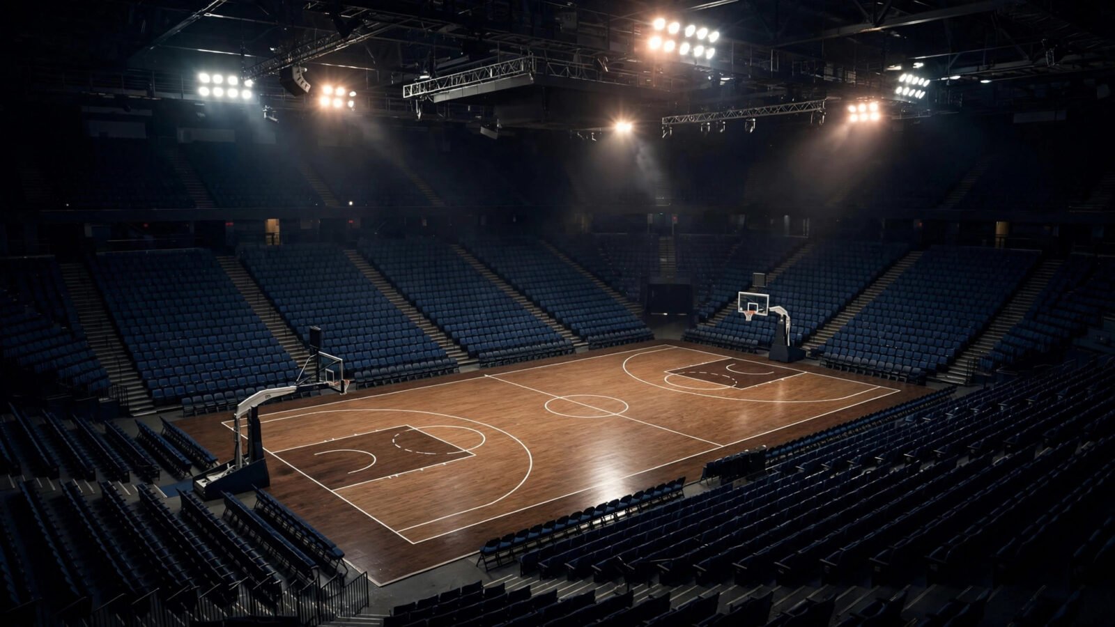 An empty basketball arena at night with a lit court and floodlights