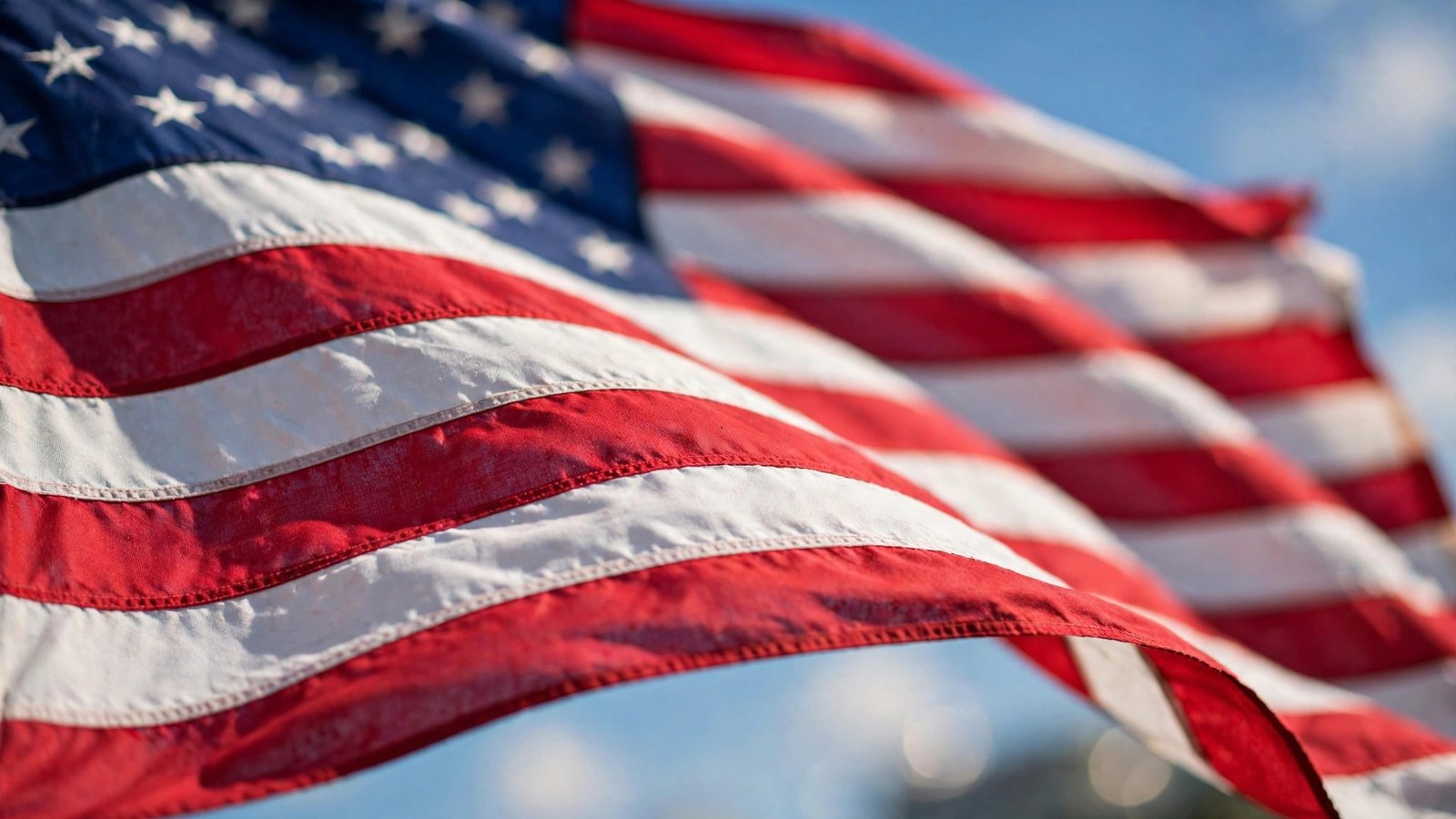 Close-up of an American flag waving in the wind against a bright blue sky