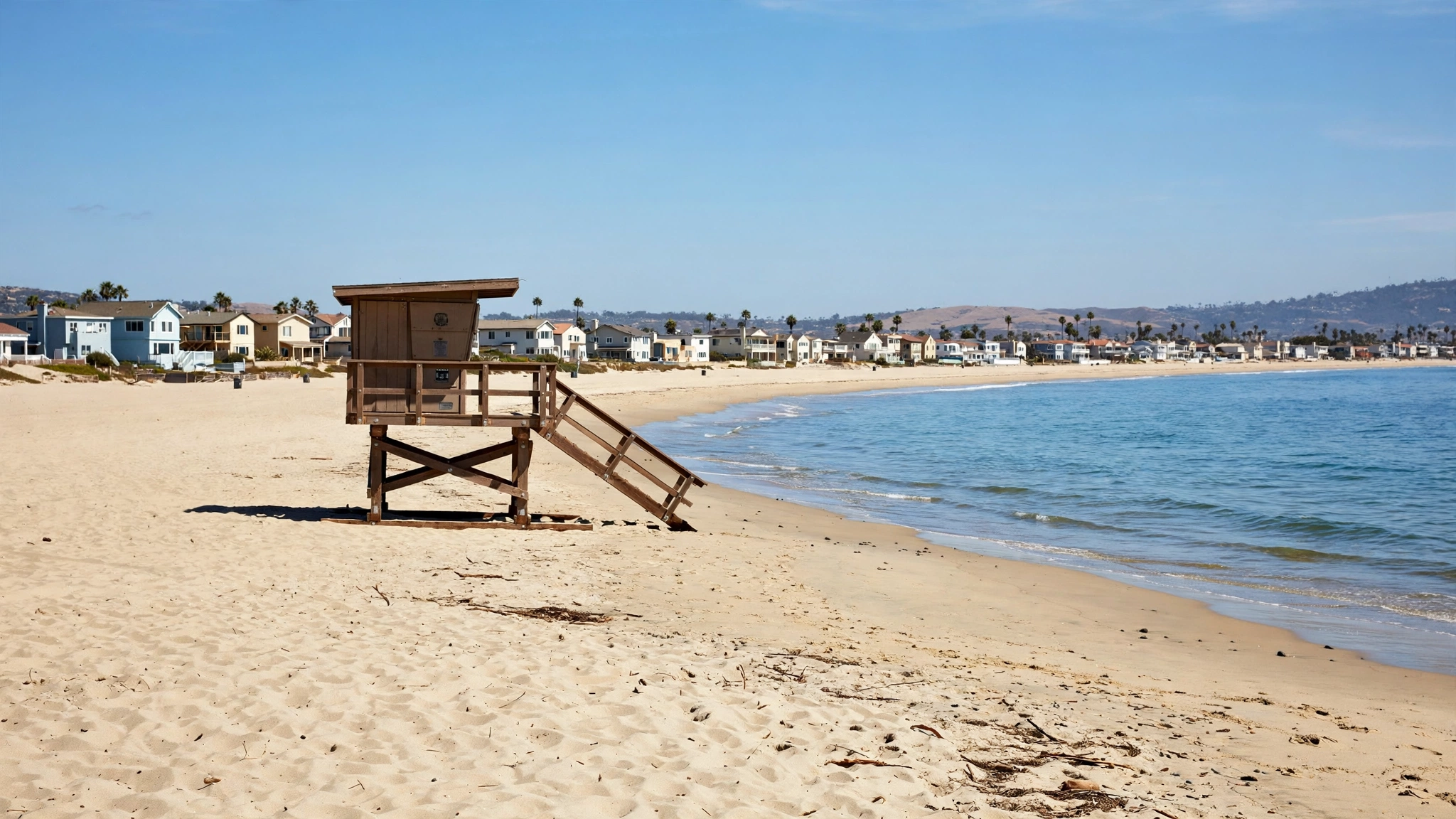 A Southern California beach with a wooden lifeguard tower and beachfront houses in the distance
