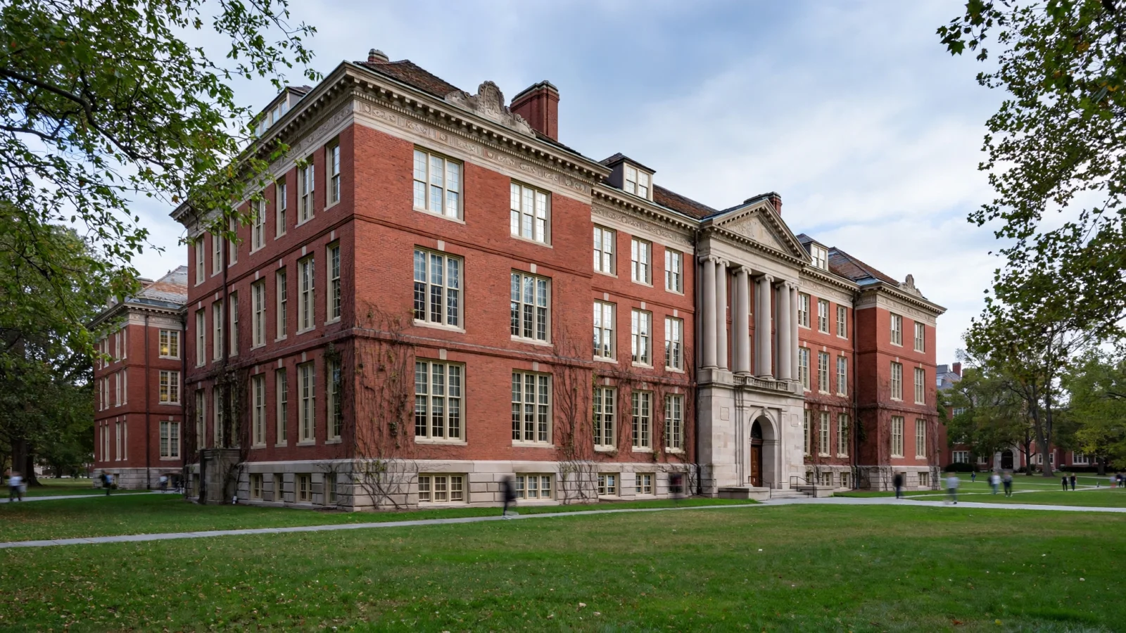 A brick university building with columns beside a lawn on a campus