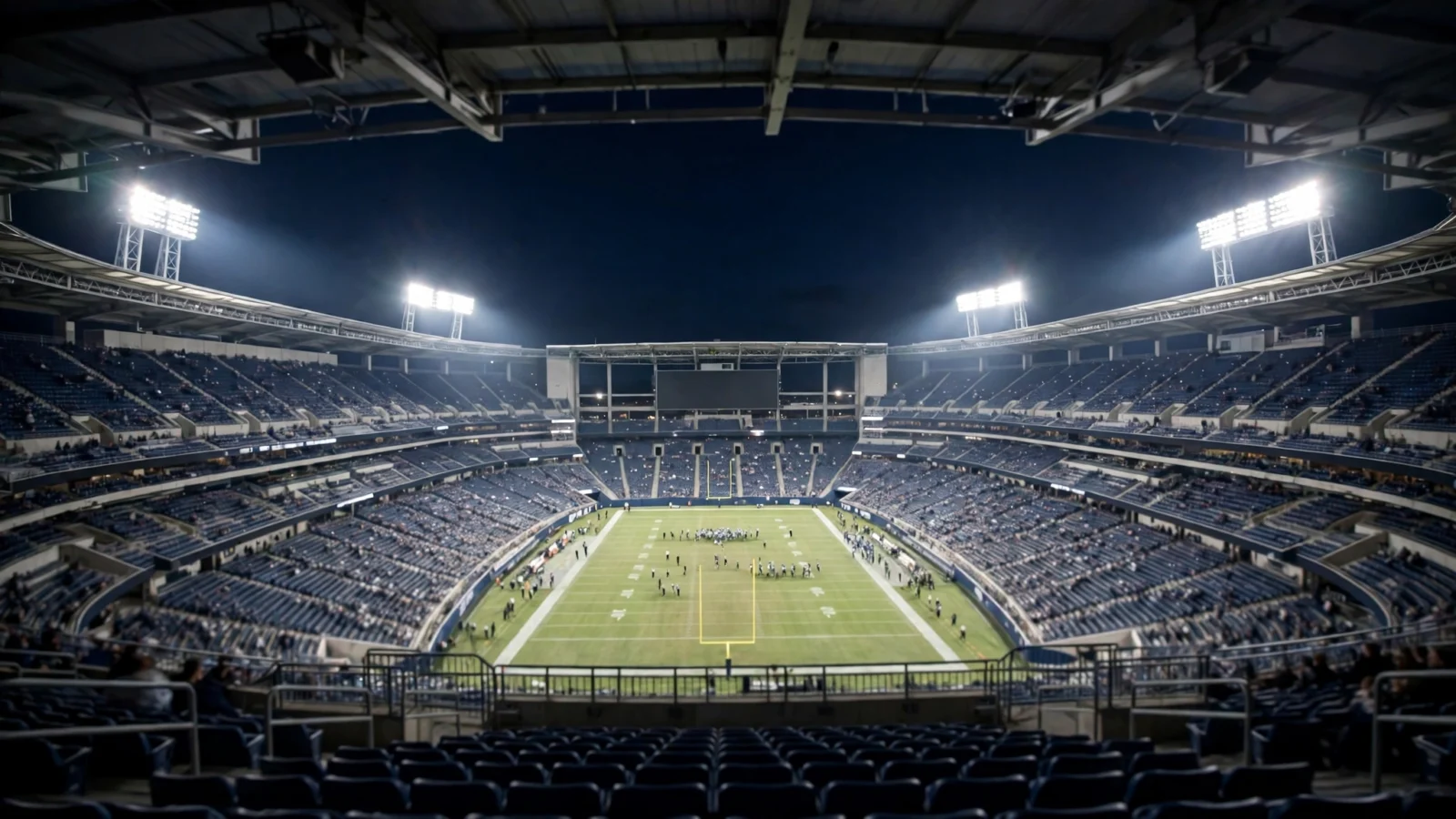 A large American football stadium lit by floodlights at night, viewed from the stands