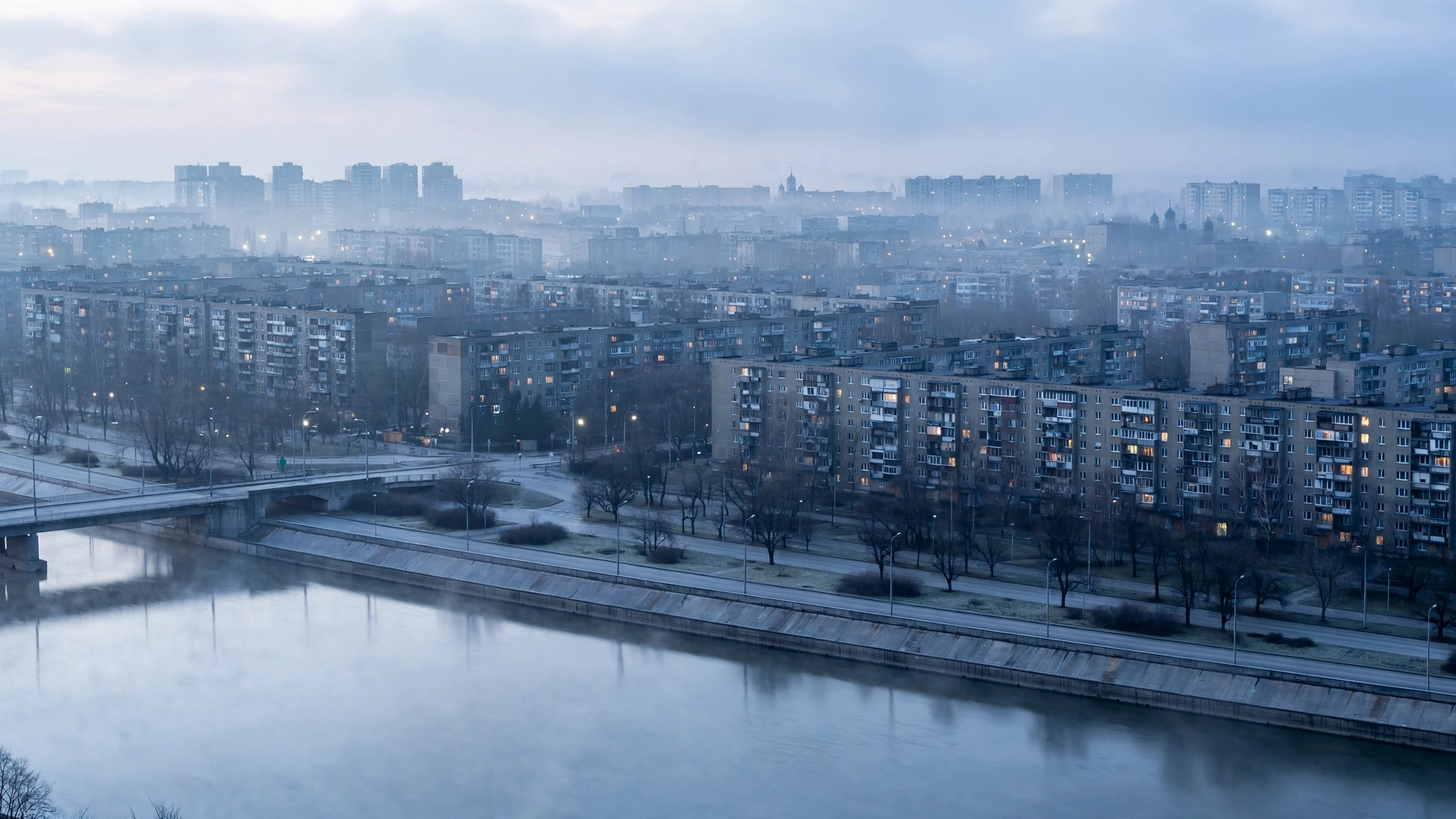 Apartment blocks and a river in a large Eastern European city at dawn, with a few lit windows