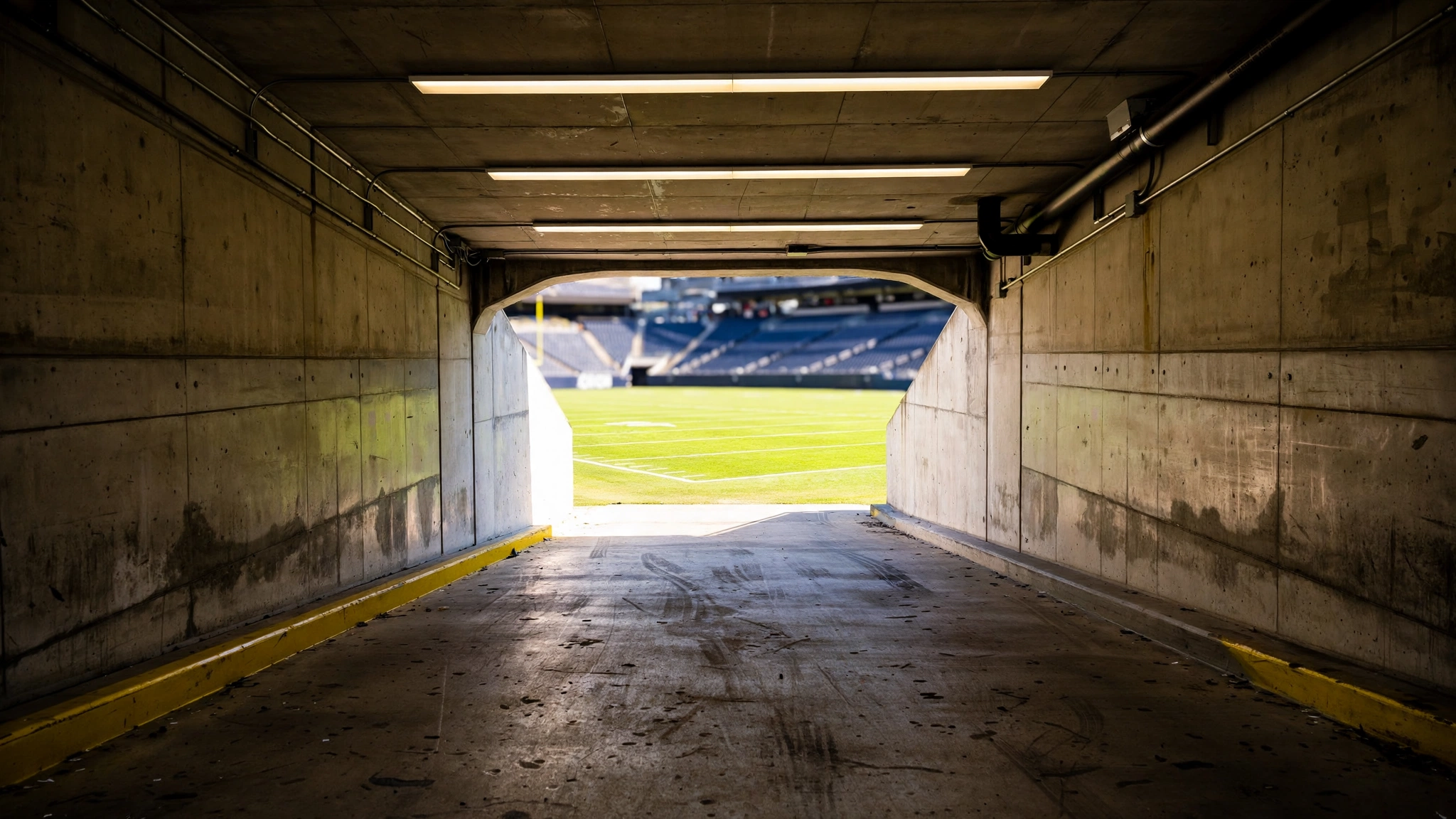 An empty concrete stadium tunnel opening onto a green football field