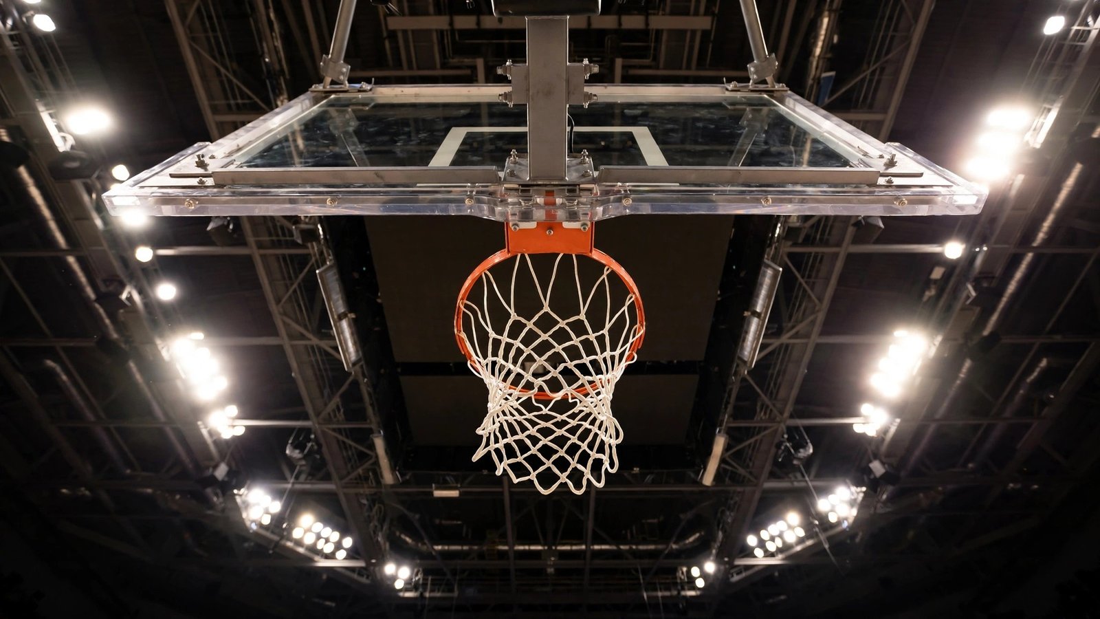 A basketball hoop and white net seen from below against arena lights