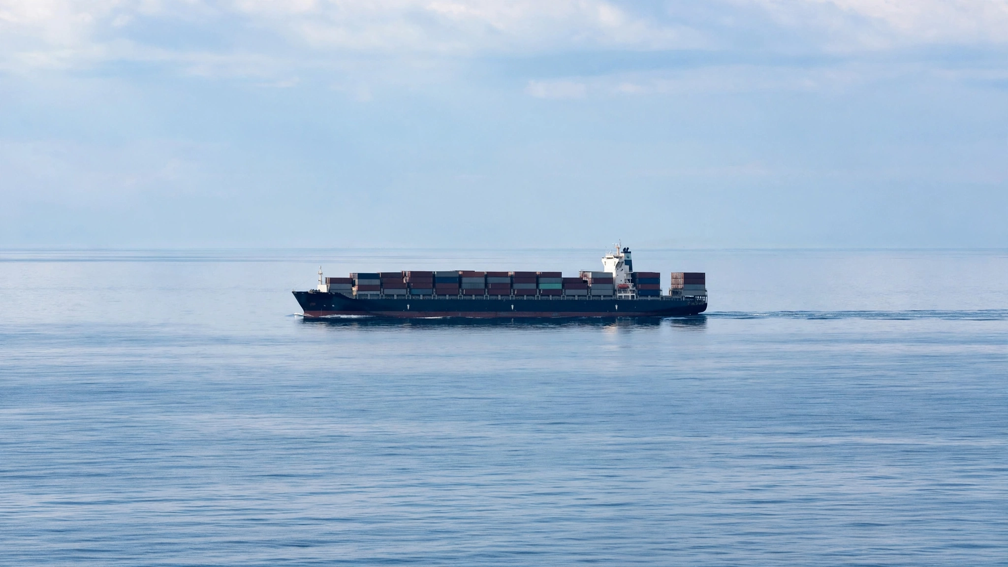 A container cargo ship carrying stacked containers across calm open water