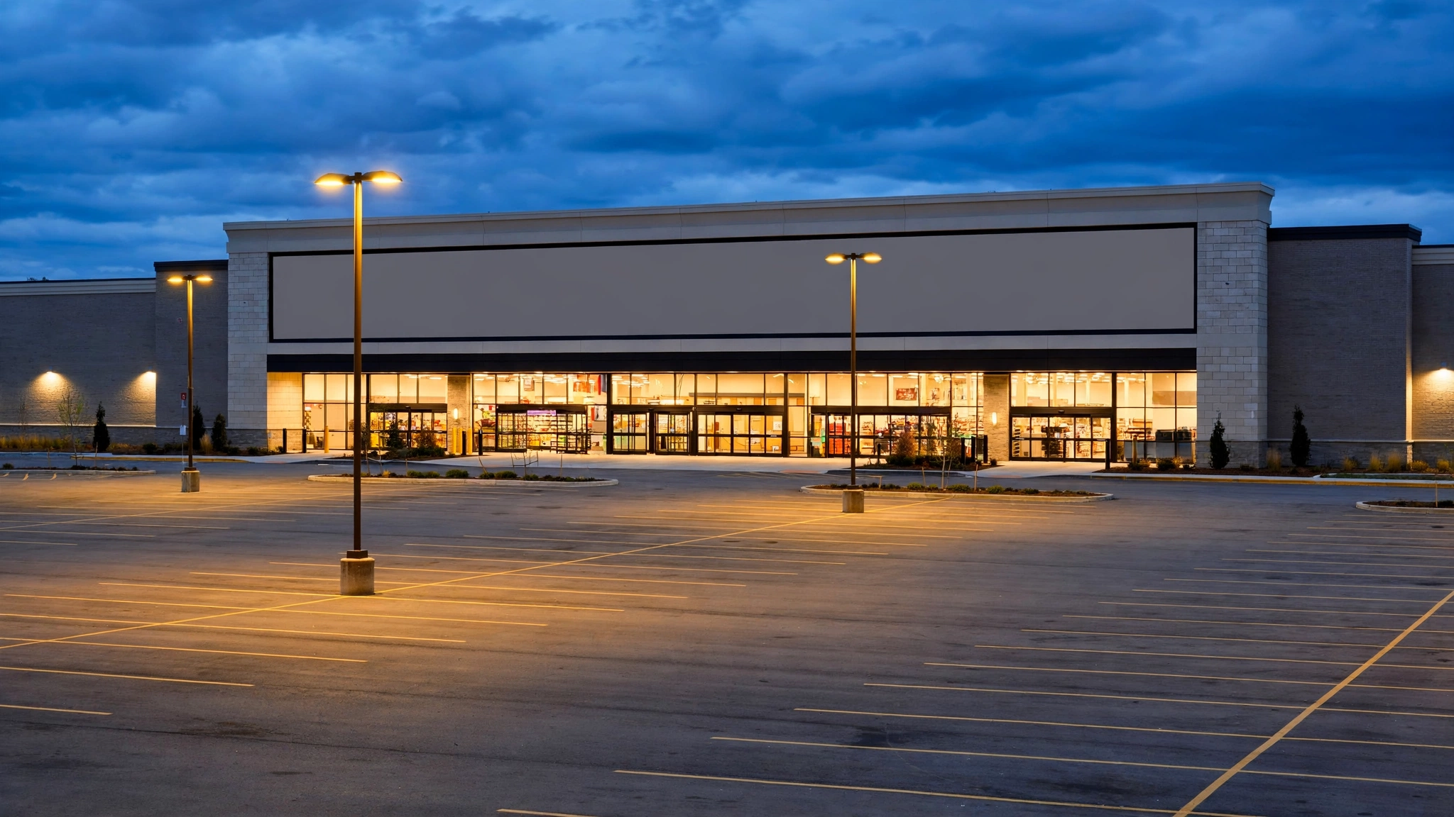 The exterior of a generic big-box retail store and empty parking lot at dusk.