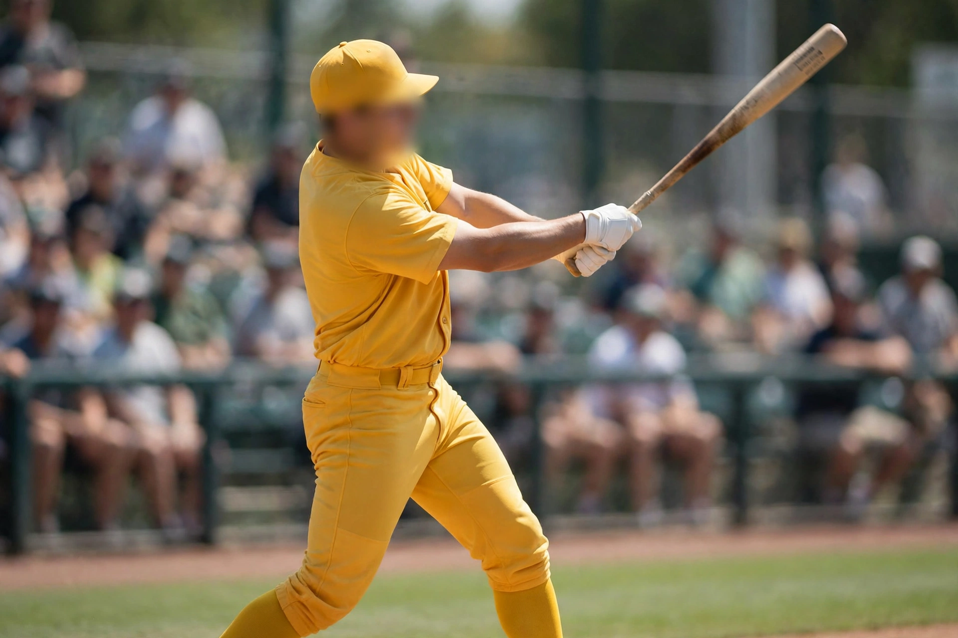 A baseball player in a plain yellow uniform swinging a bat during a daytime game, with blurred fans in the background.