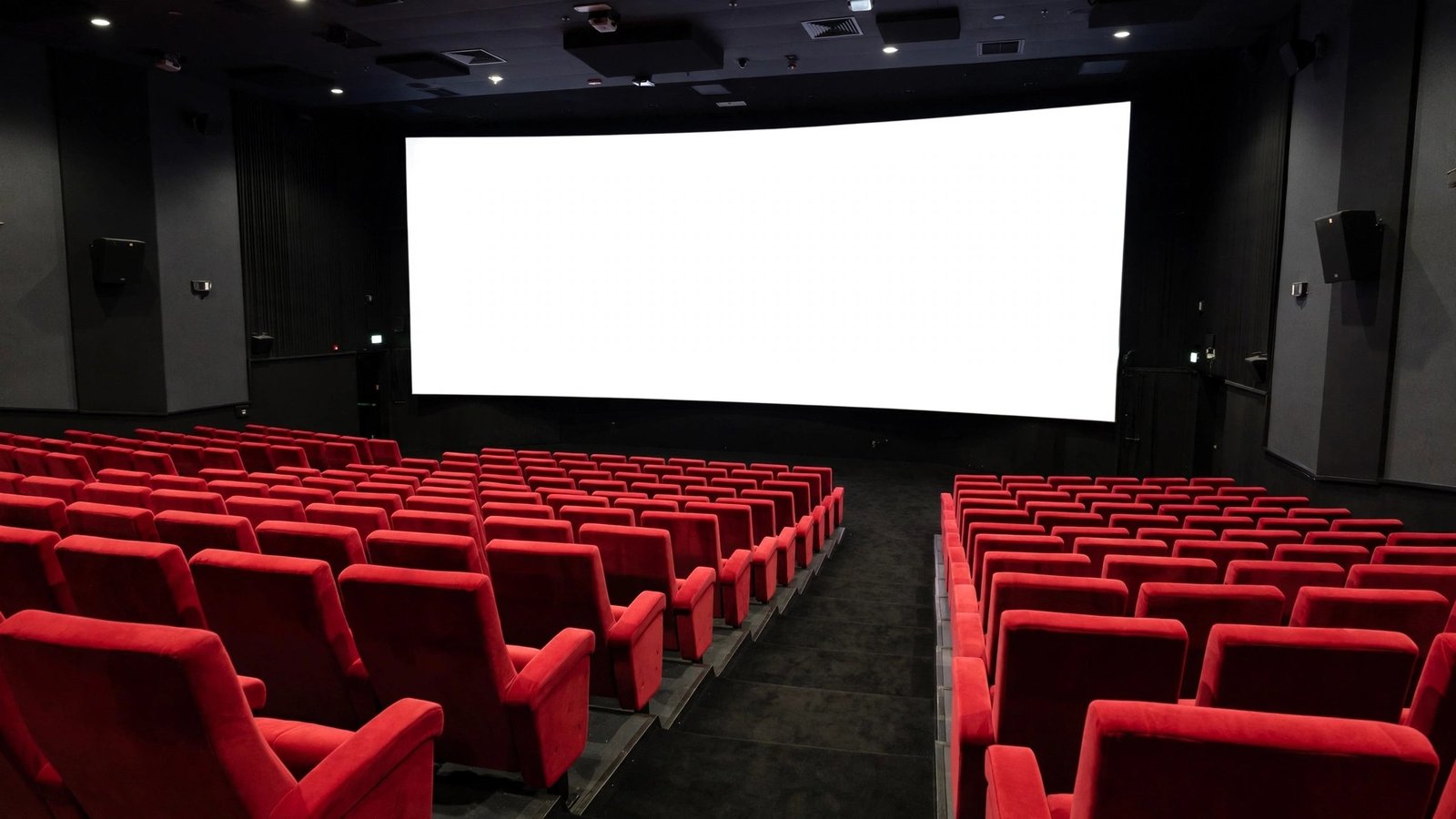 An empty cinema auditorium with red seats and a blank white screen