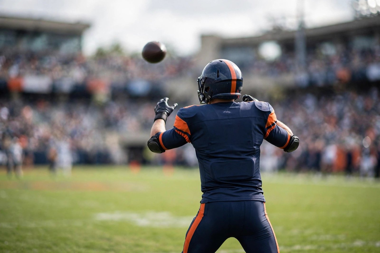 A quarterback in a navy-blue and orange uniform seen from behind throwing a football during a daytime game