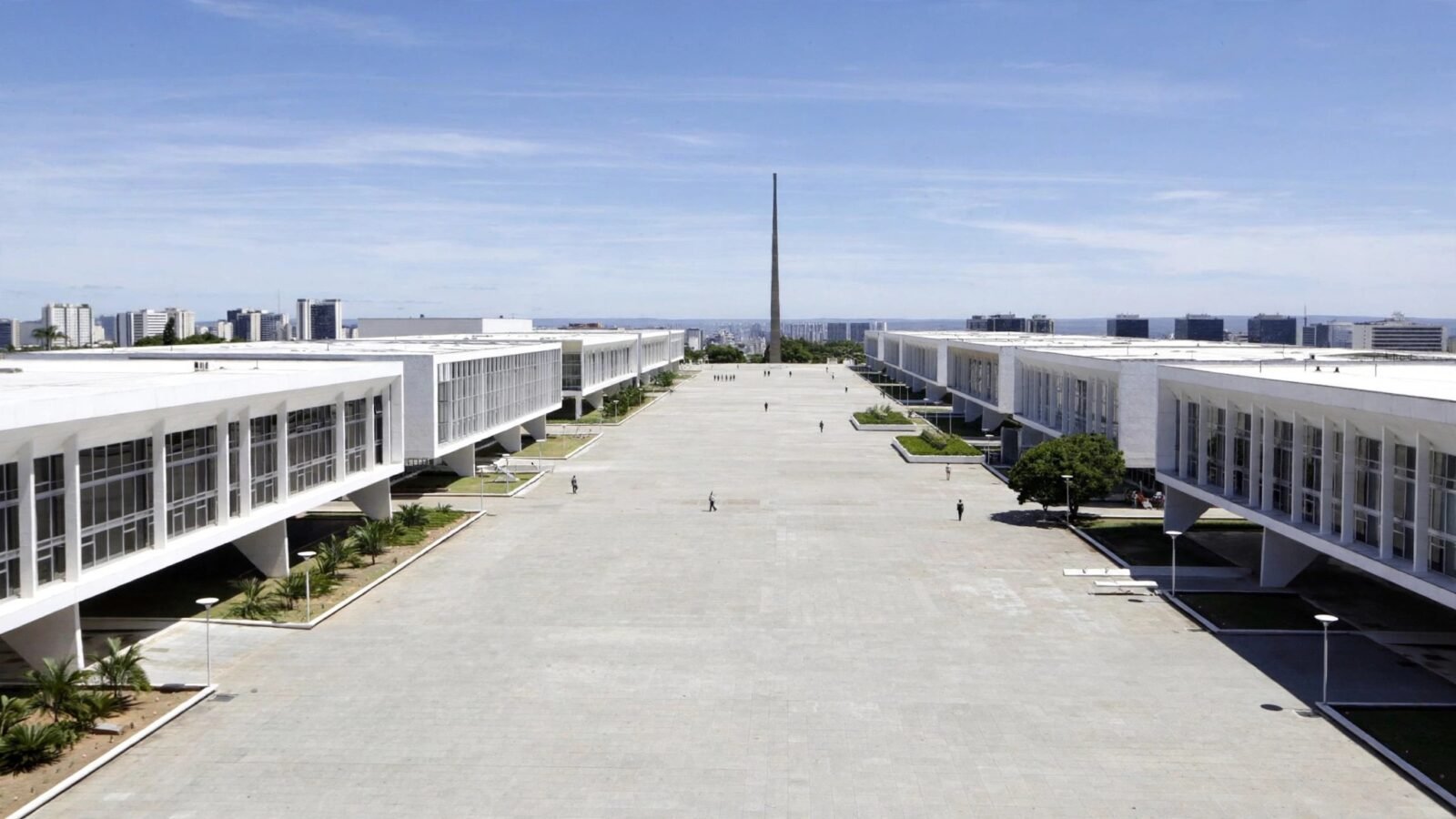 A wide government plaza in Brasilia lined with white modernist ministry buildings under a clear sky