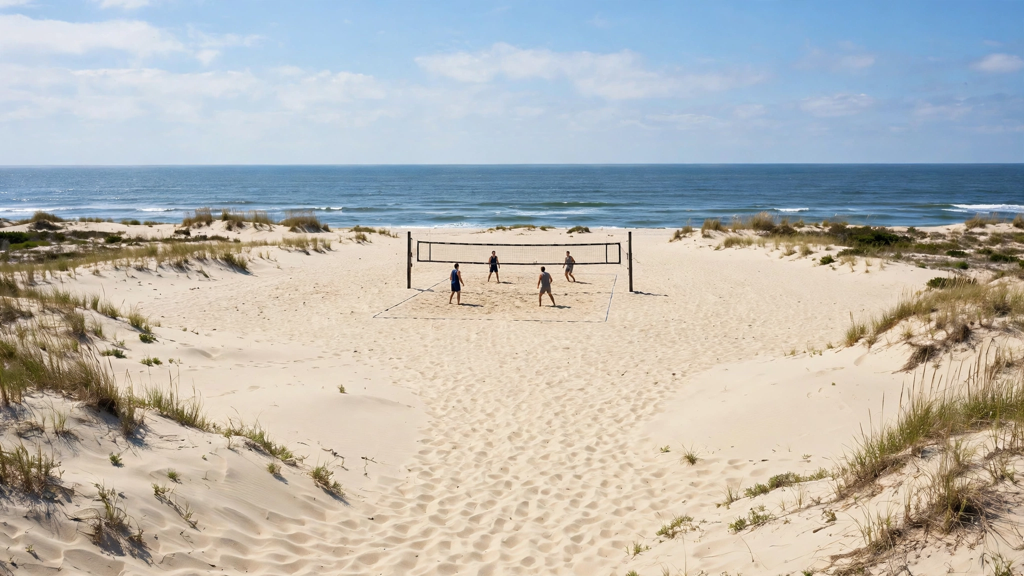 Four people playing beach volleyball on a sandy court beside the ocean